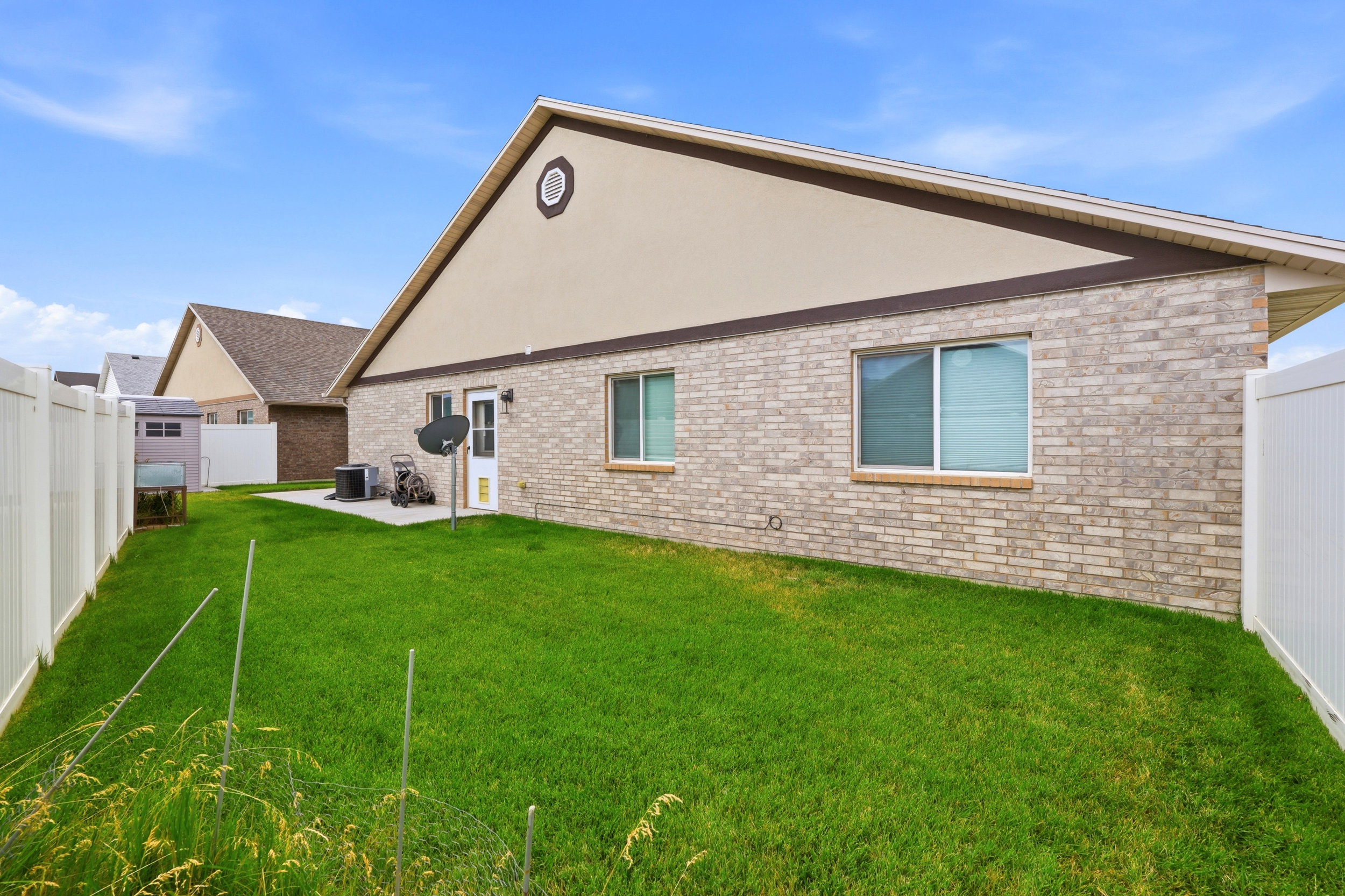 Expansive grassy backyard featuring a full vinyl fence, brick and stucco exterior, and a concrete patio