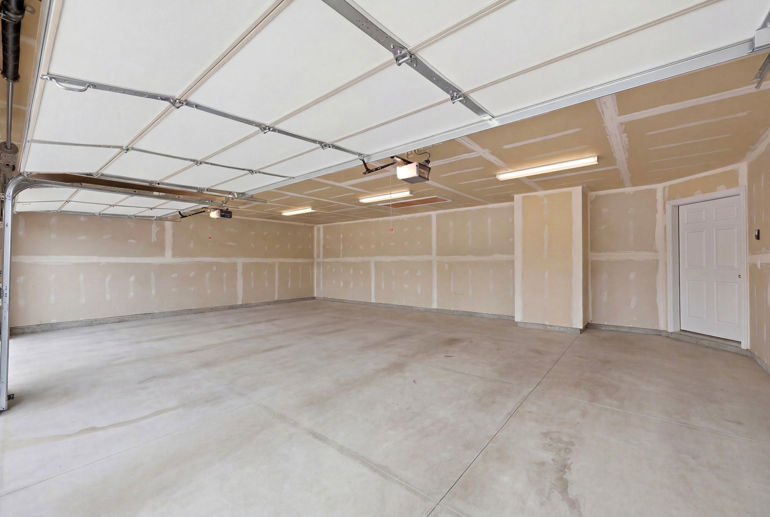 Spacious garage featuring a concrete floor, exposed drywall walls, fluorescent lighting, and a white interior door