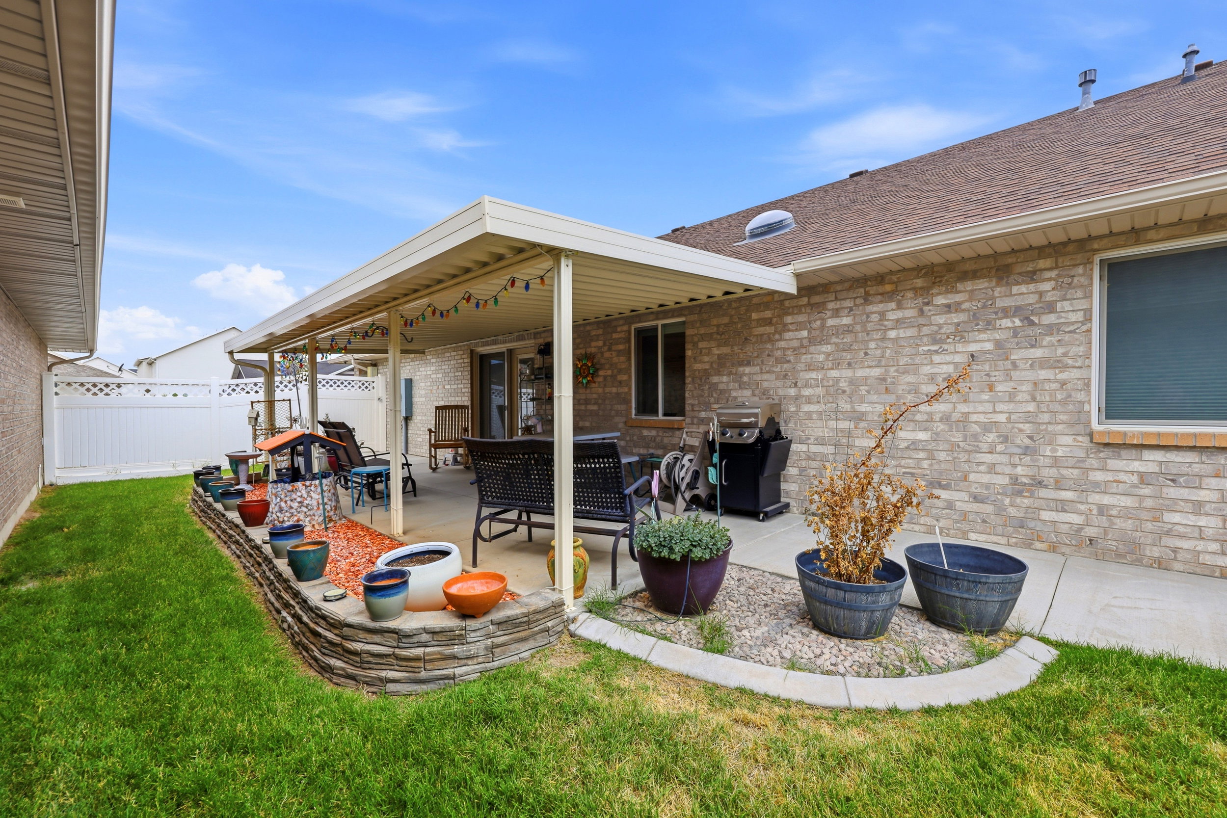 Expansive covered patio featuring a concrete surface, brick exterior, and a stone-stacked raised garden bed