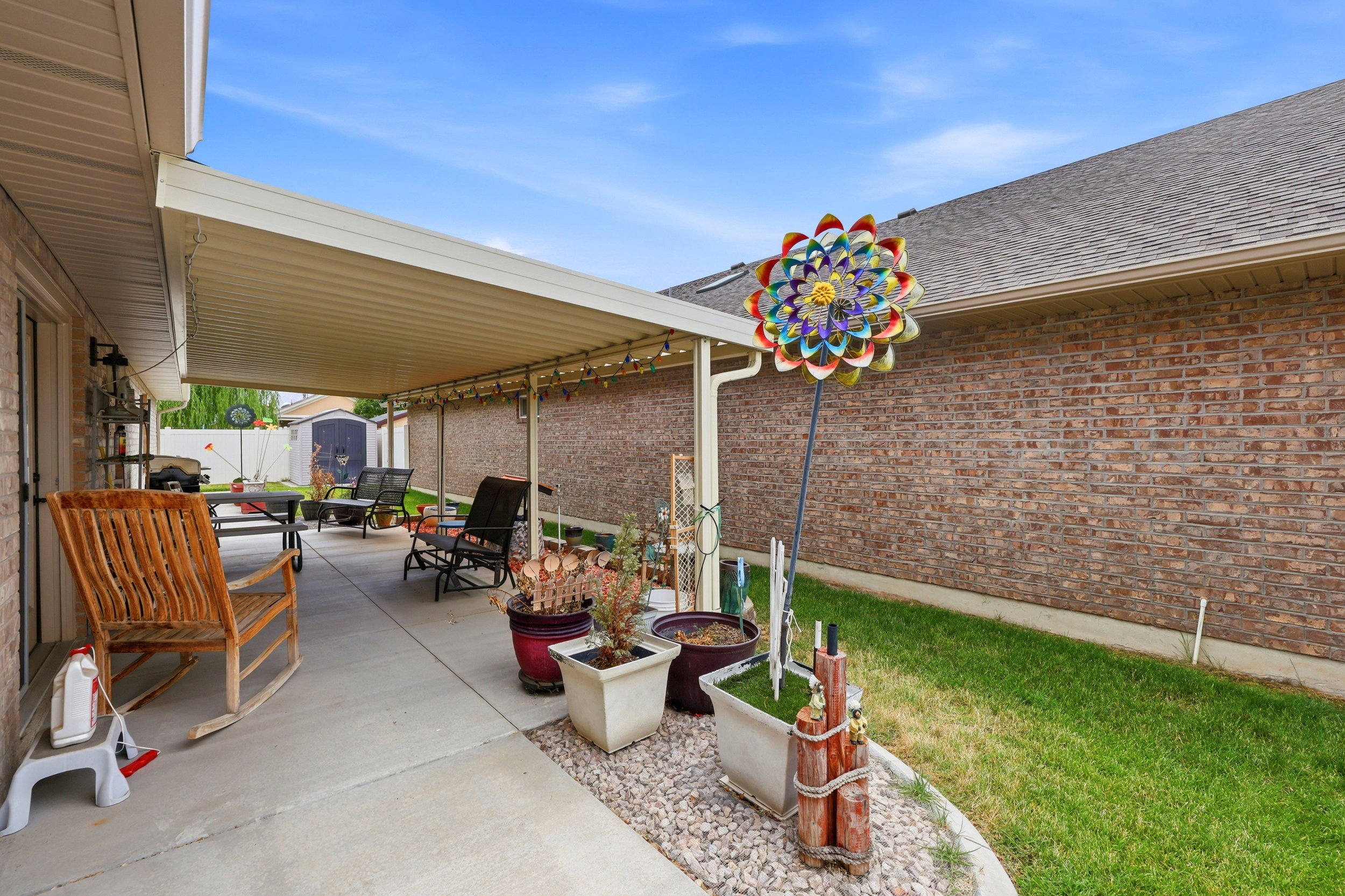 Covered concrete patio with a brick exterior, stone aggregate border, and a grass area