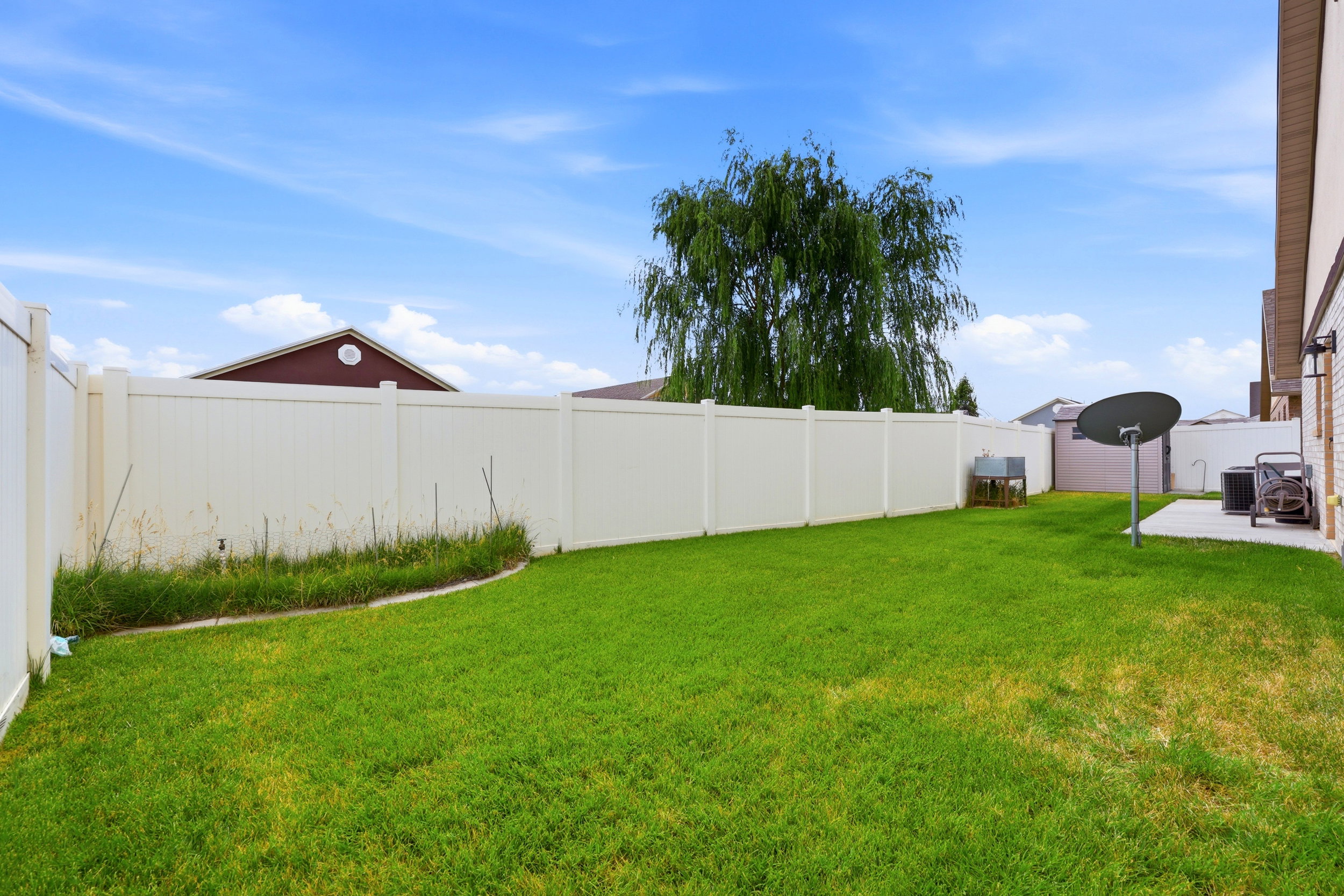 Expansive backyard featuring a green lawn, full perimeter fencing, mature tree, and a concrete patio