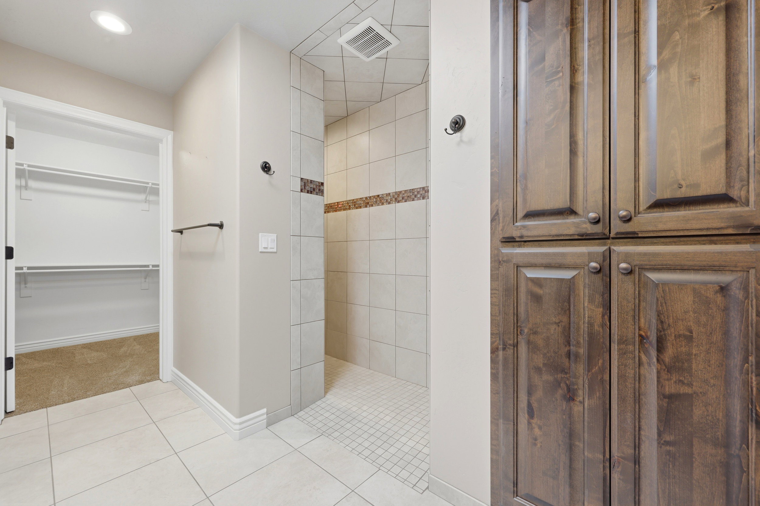 Spacious walk-in shower featuring light-colored tile and decorative accent band
