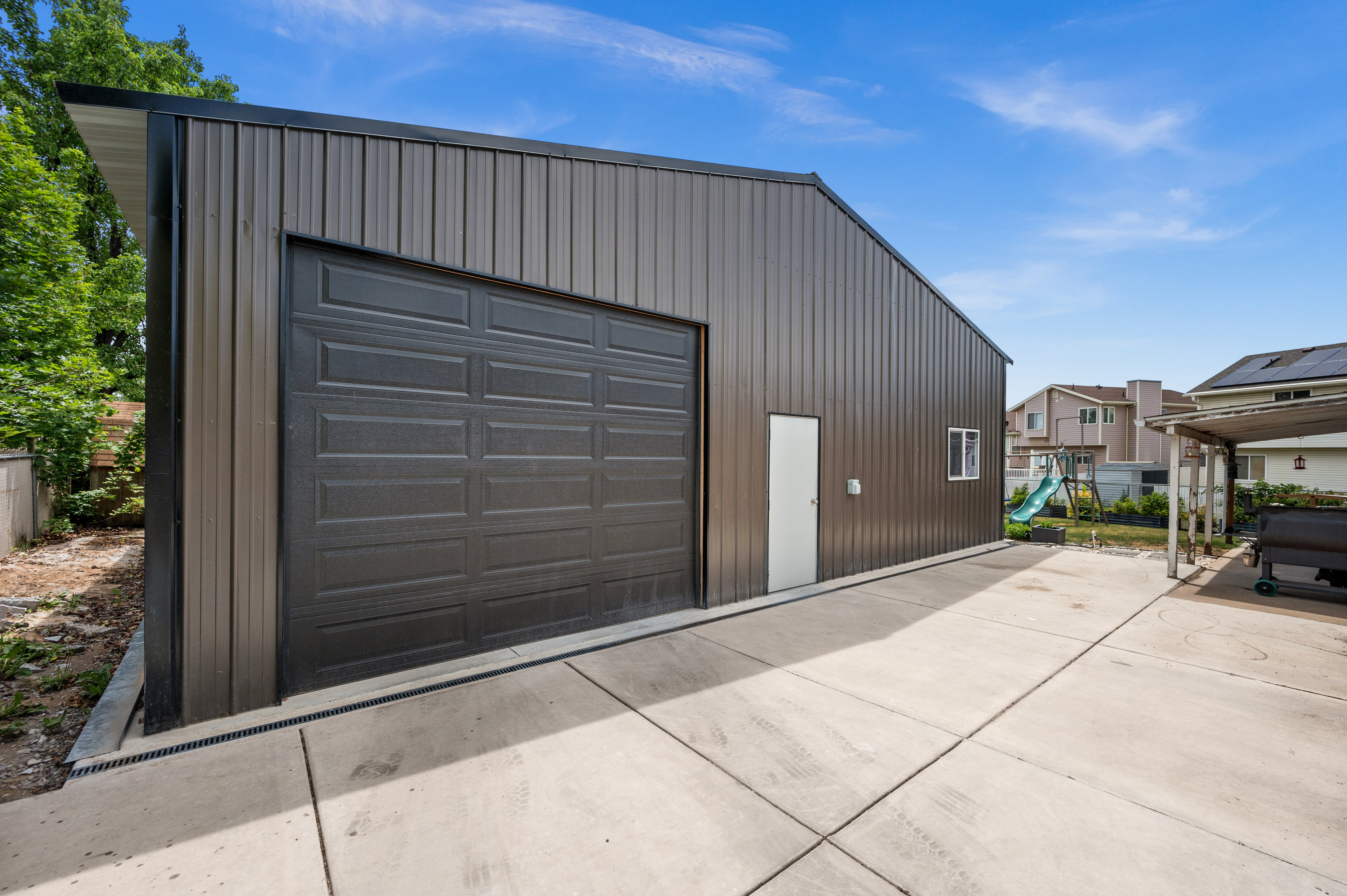 Detached metal utility building featuring a dark paneled garage door and a separate entry door