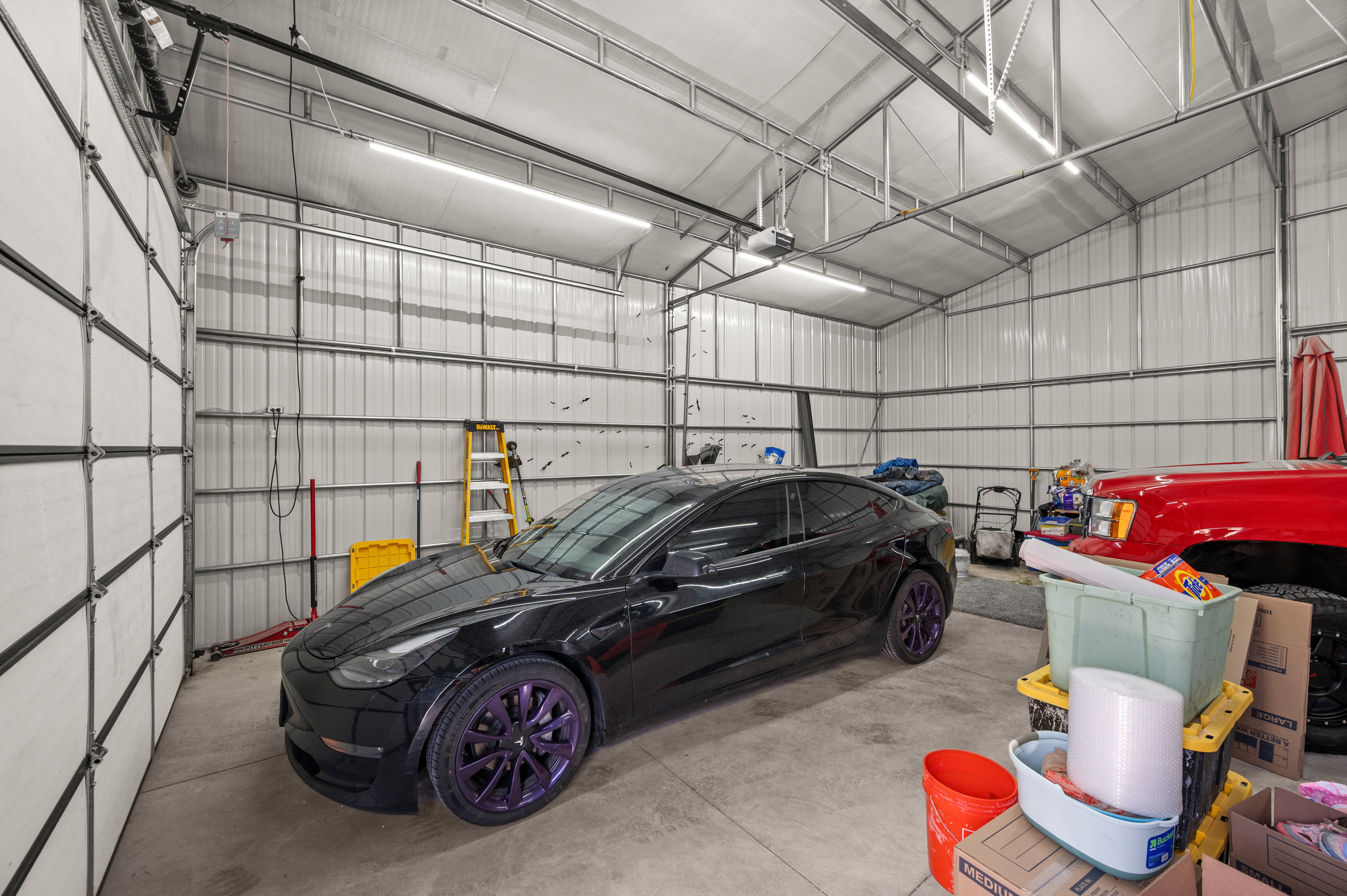 Spacious metal-sided garage featuring a concrete floor, multiple fluorescent light fixtures, and overhead garage door system
