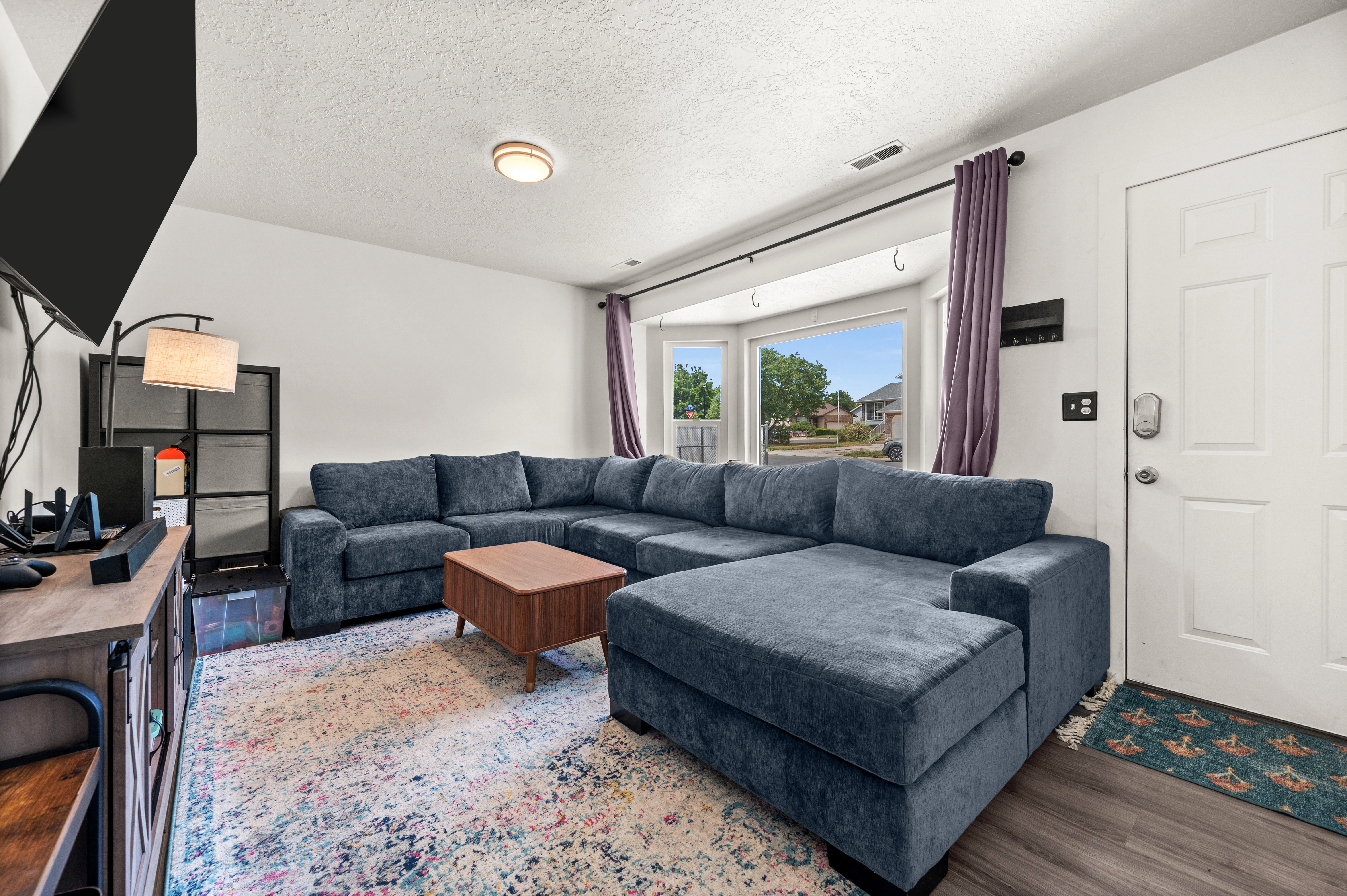 Living area featuring a bay window, wood-finish flooring, white paneled entry door, and recessed ceiling lighting
