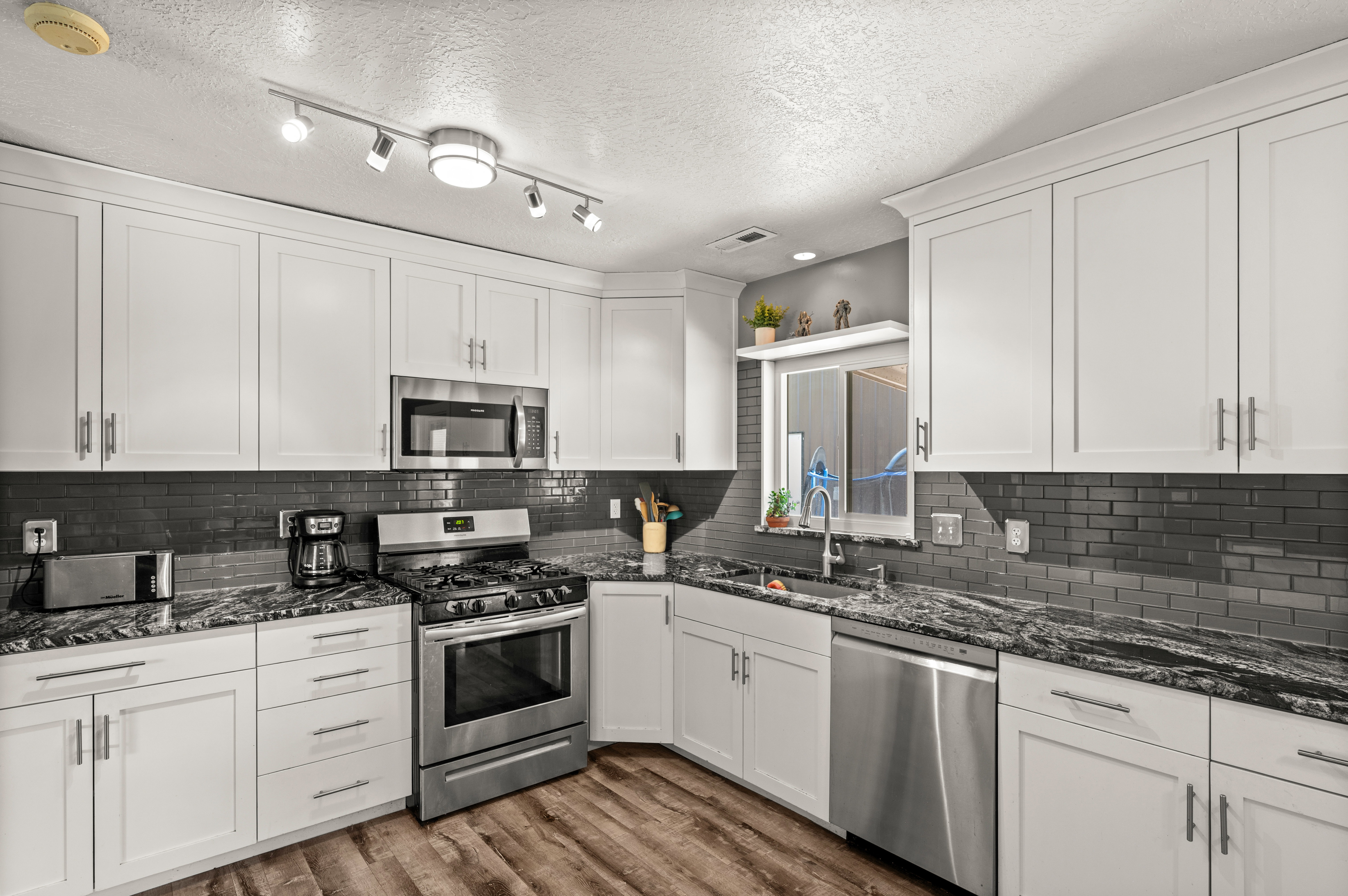 Kitchen featuring white cabinetry, dark subway tile backsplash, stainless steel appliances, dark patterned countertops, and wood-finish flooring