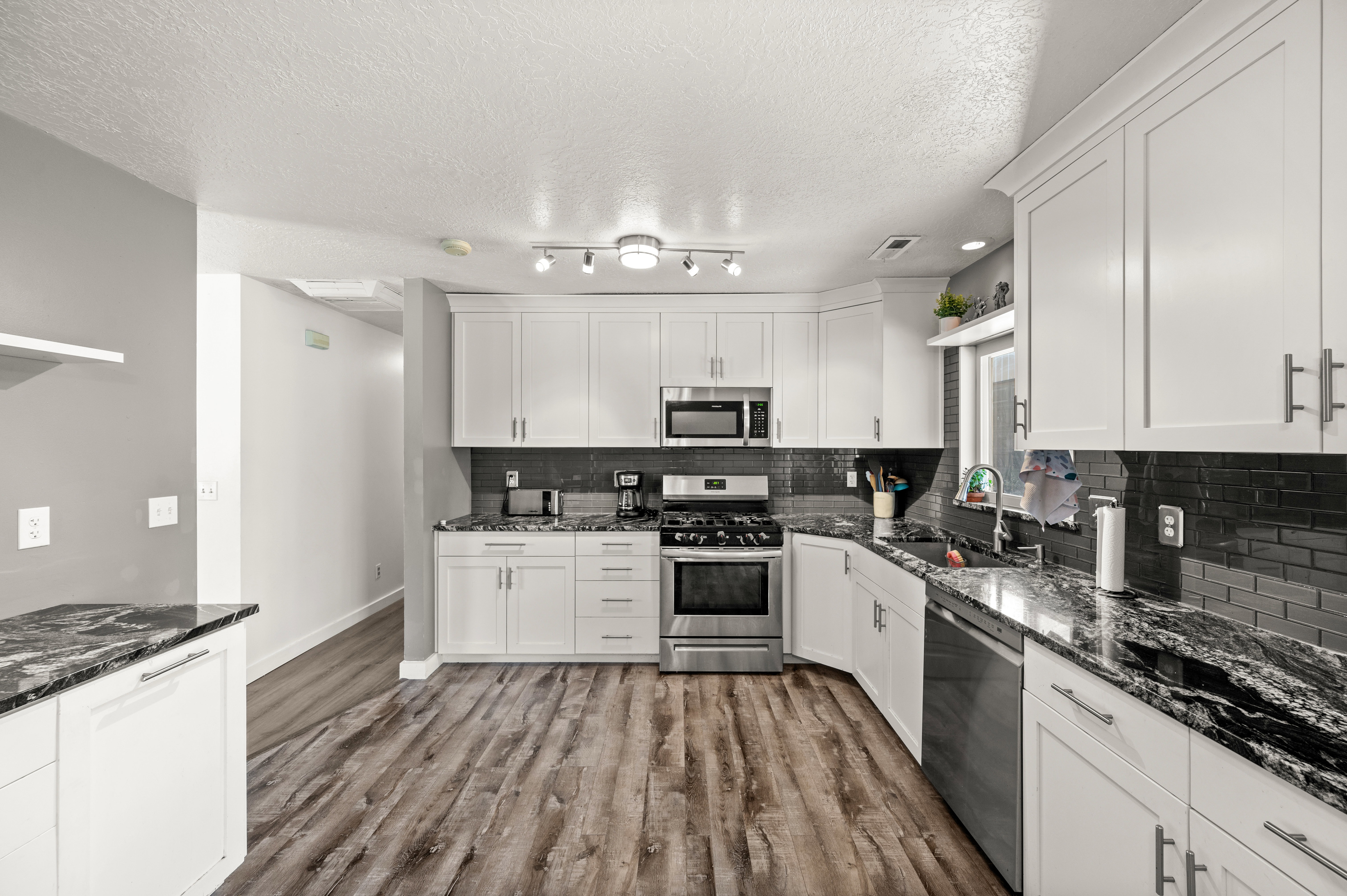 Kitchen featuring white shaker cabinetry, stainless steel appliances, dark subway tile backsplash, stone countertops, and wood-finish flooring