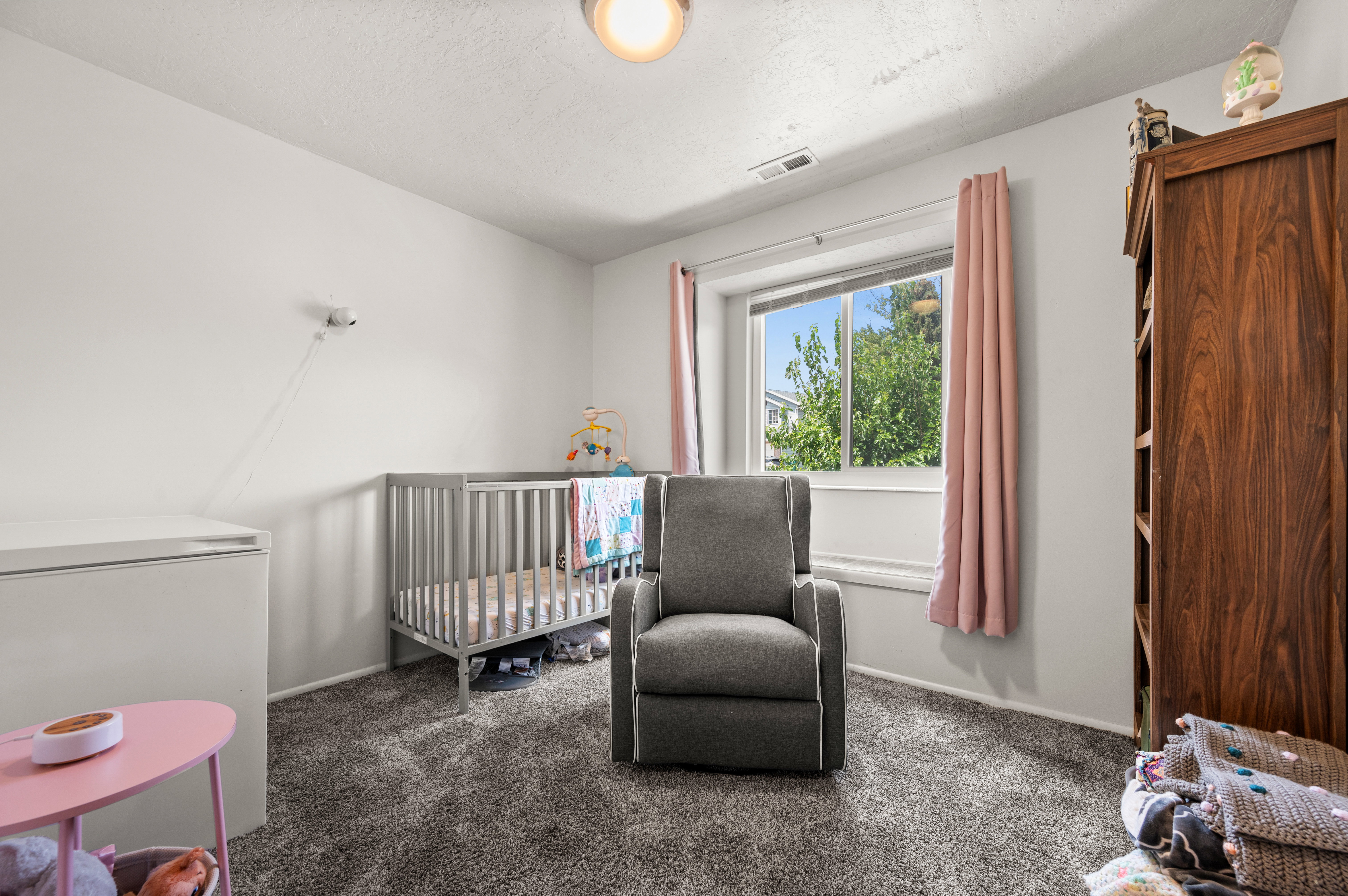 Neutral wall paint with textured carpeting, a window featuring exterior landscaping, and a ceiling light fixture