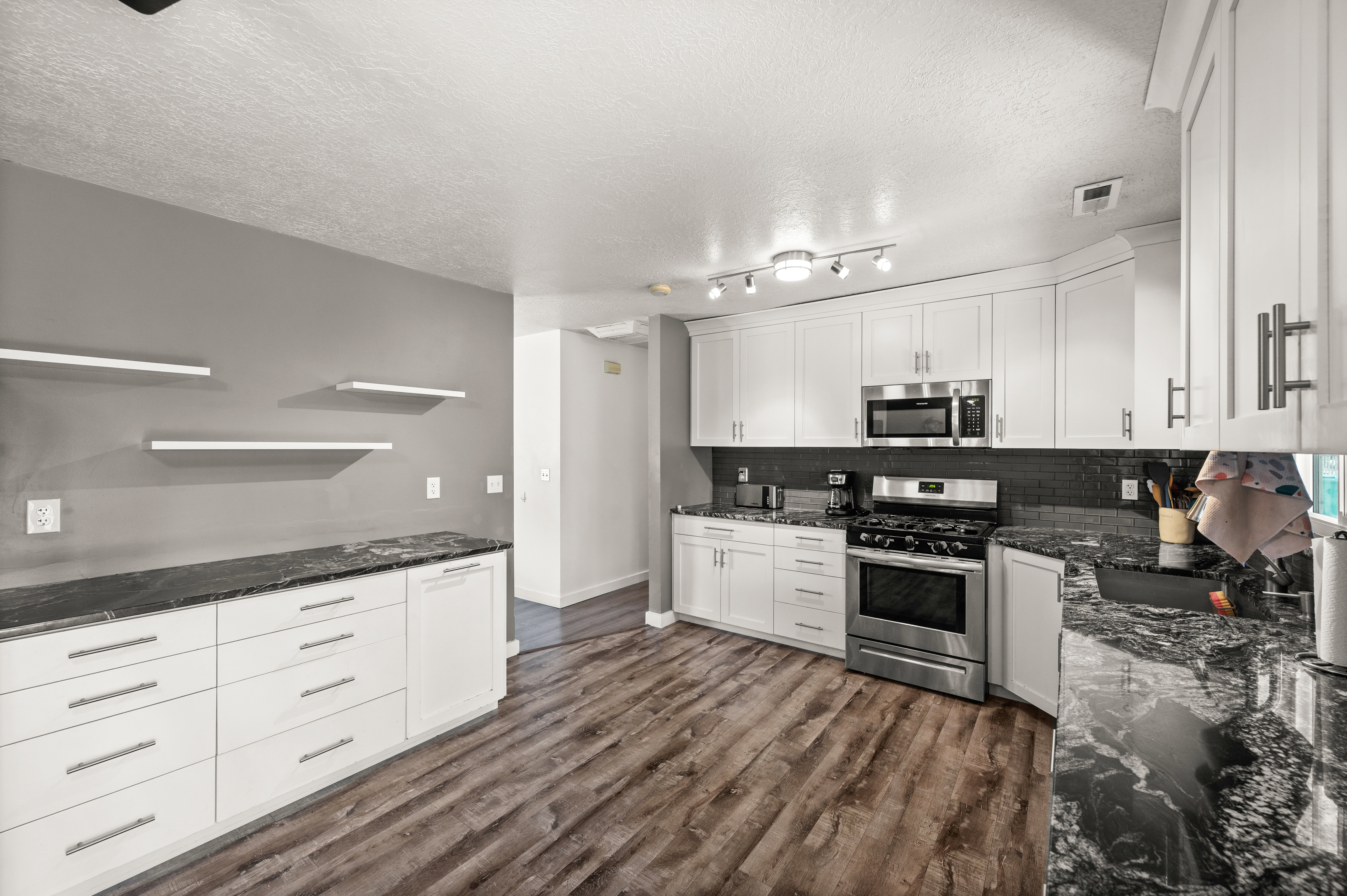Kitchen featuring white cabinetry, dark stone countertops, stainless steel appliances, dark tile backsplash, and wood-finish flooring