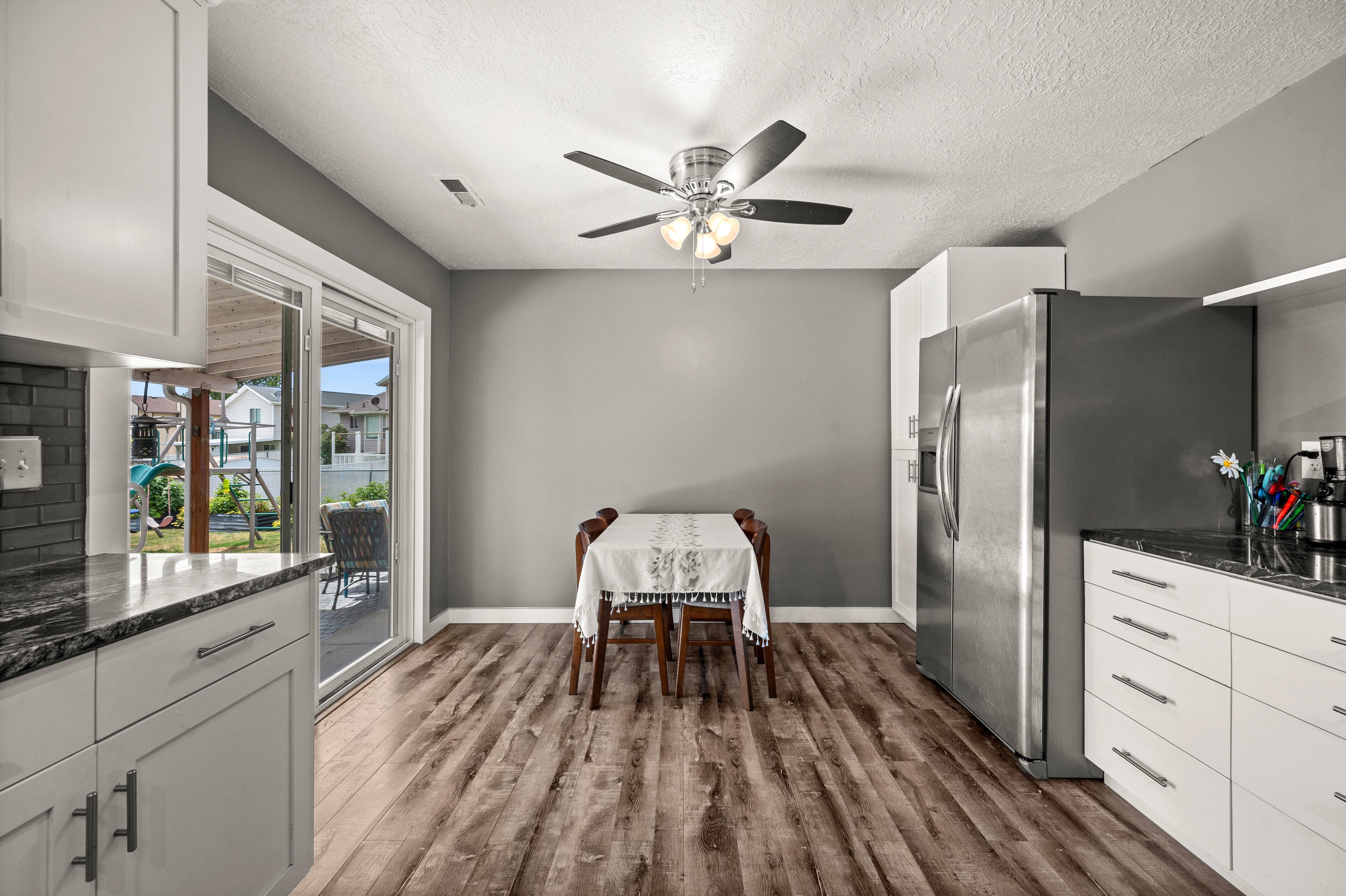 Open-concept kitchen and dining area featuring wood-finish flooring, white cabinetry, dark stone-finish countertops, and a sliding glass door providing access to the exterior