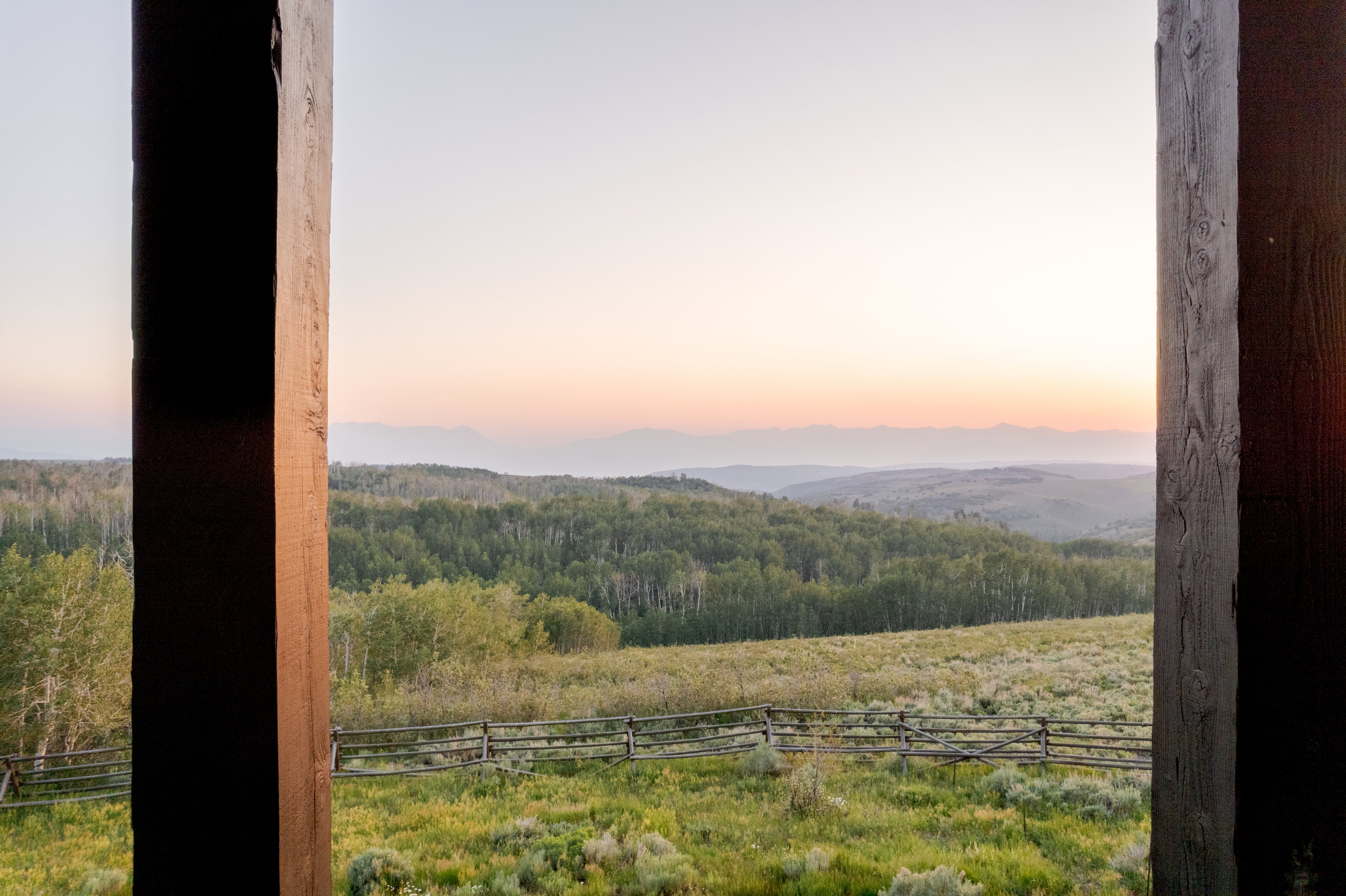 Expansive natural landscape with rolling hills, a lush green field, and dense forestation