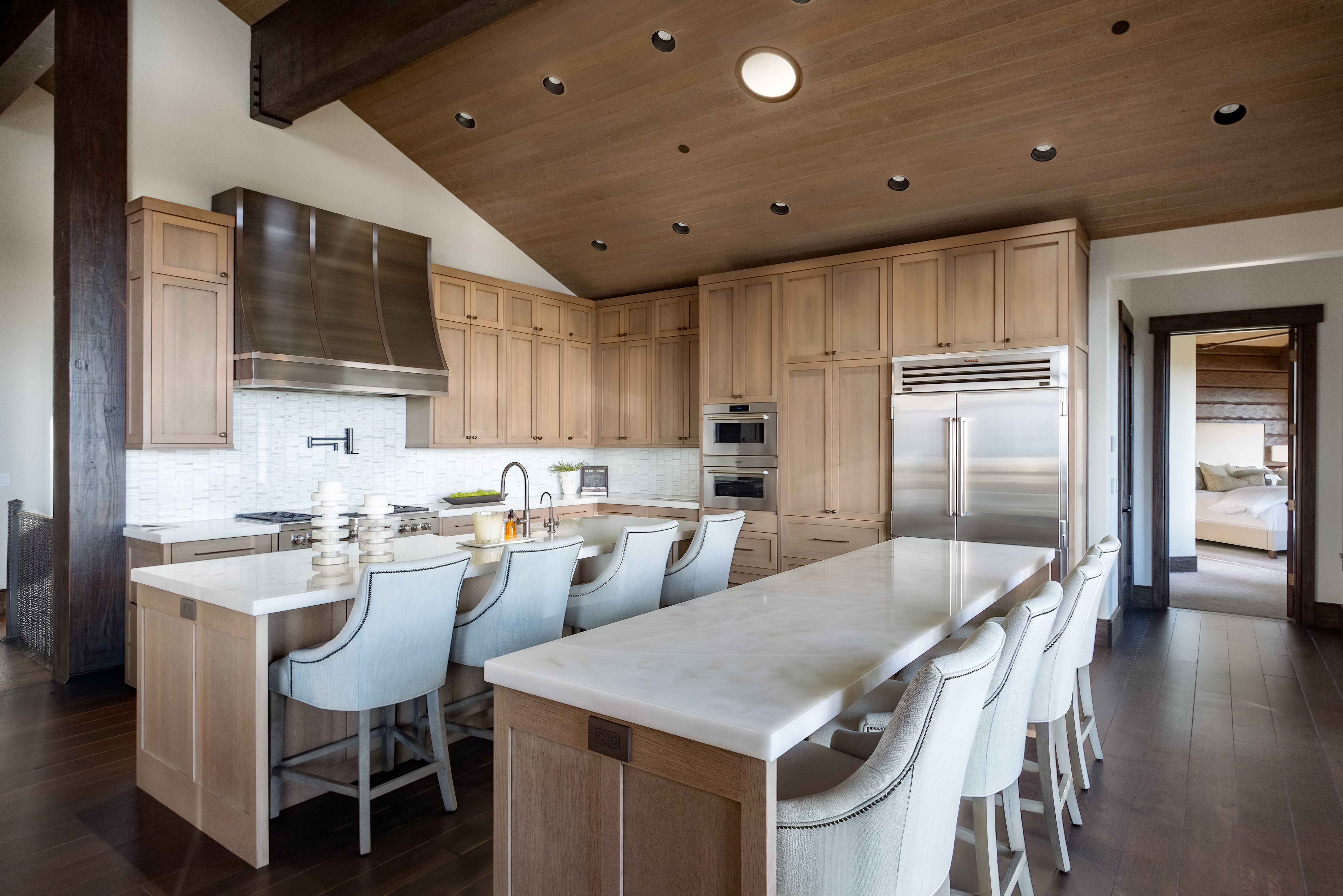 Gourmet kitchen featuring a large central island with seating, stainless steel appliances, extensive cabinetry, light wood-finish flooring, and a vaulted wood-paneled ceiling