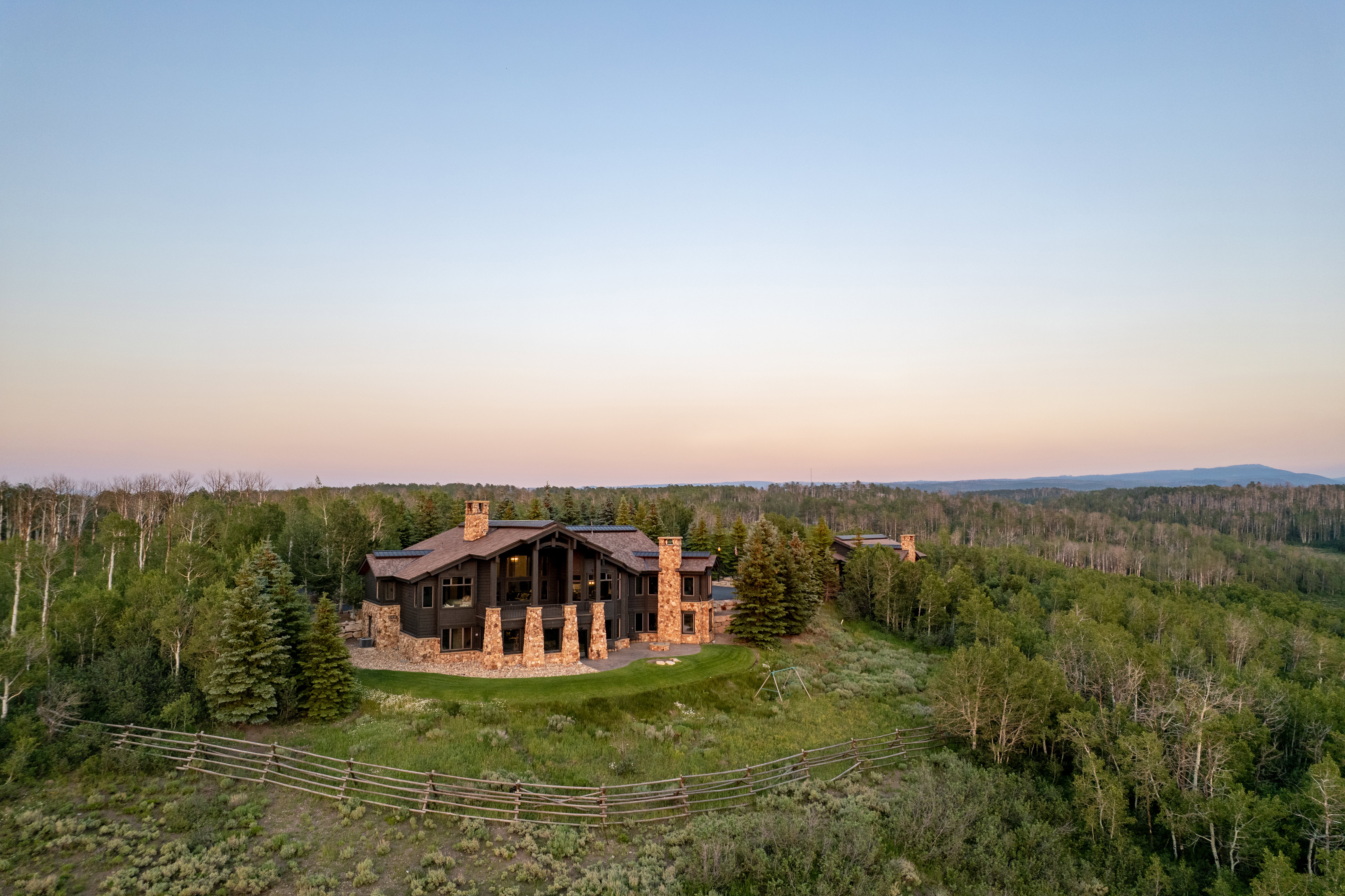 Expansive property featuring a multi-level residence with stone and dark wood siding, multiple chimneys, and a stone retaining wall