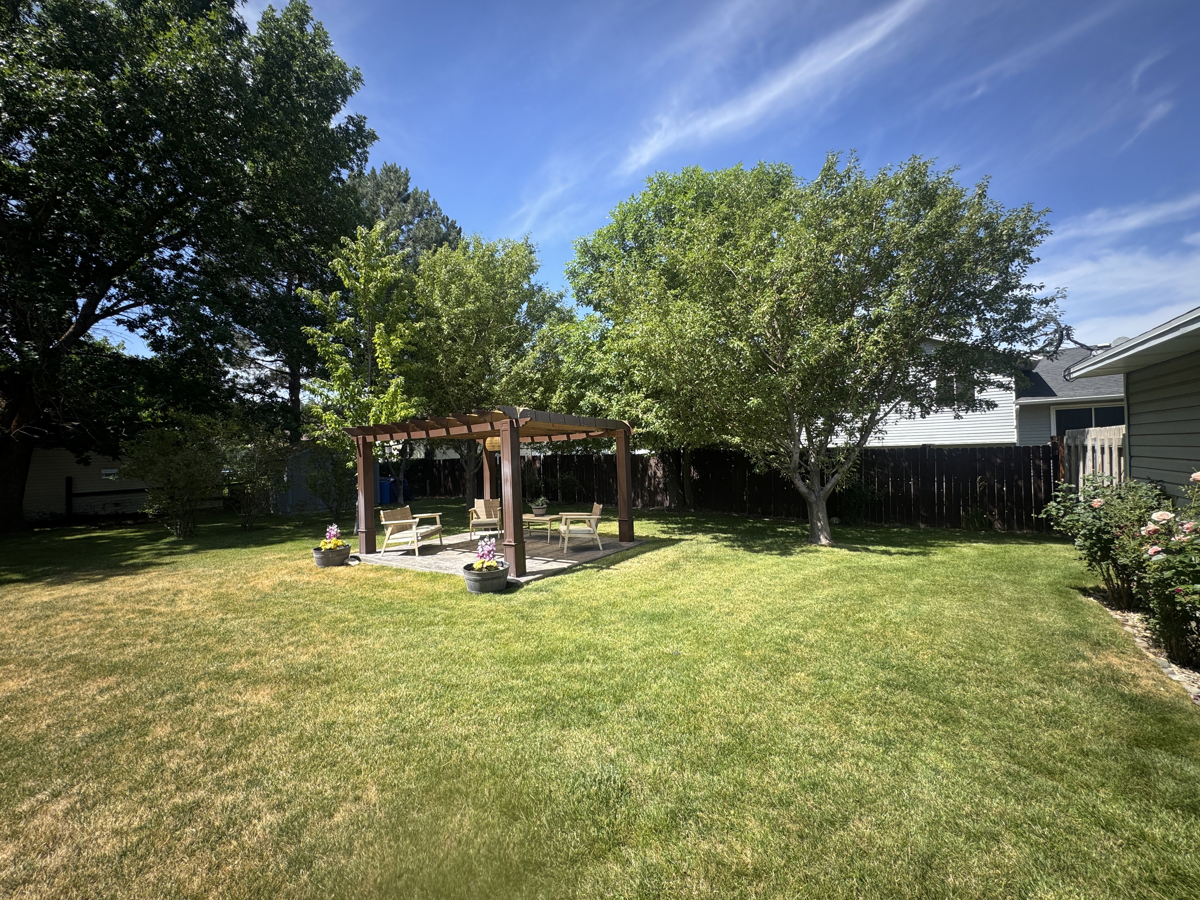 Spacious backyard featuring a wood pergola over a paved patio