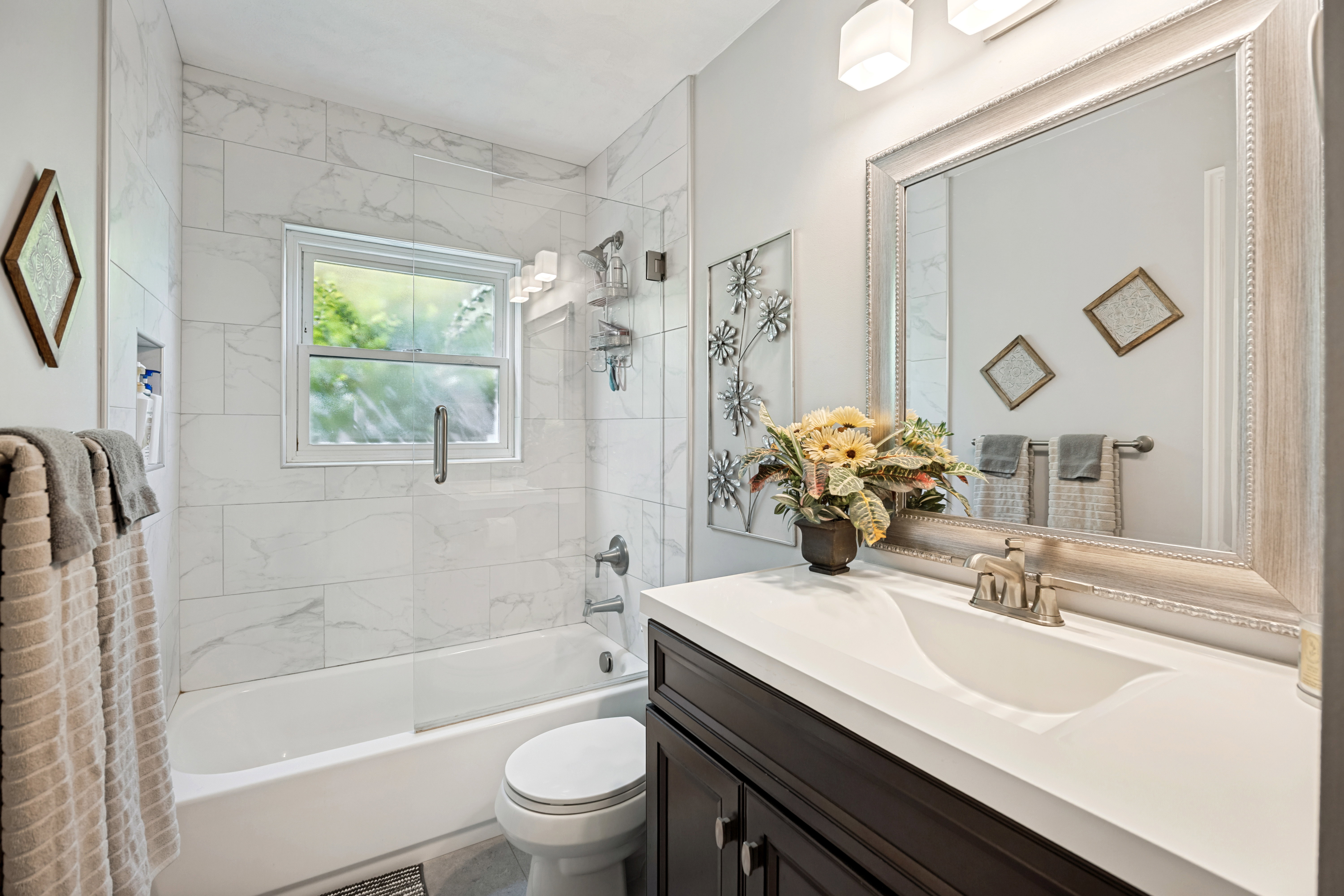 Bathroom featuring a dark wood vanity with white countertop and integrated sink, a large framed mirror, and a tub-shower combination with white tile surround