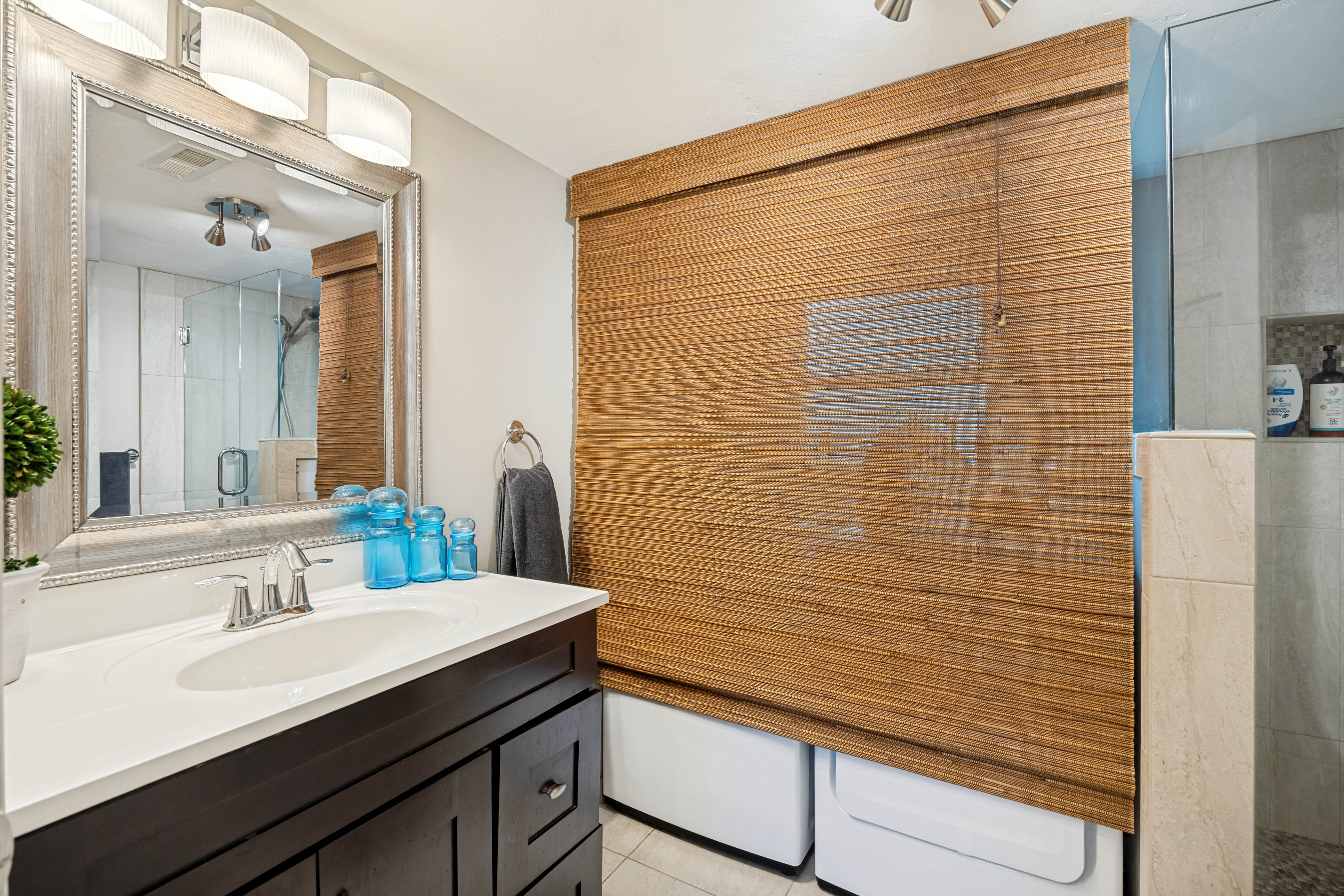 Bathroom featuring a dark wood-finish vanity with a white countertop and undermount sink, a large framed mirror with overhead lighting, and a walk-in shower with glass enclosure and tiled walls