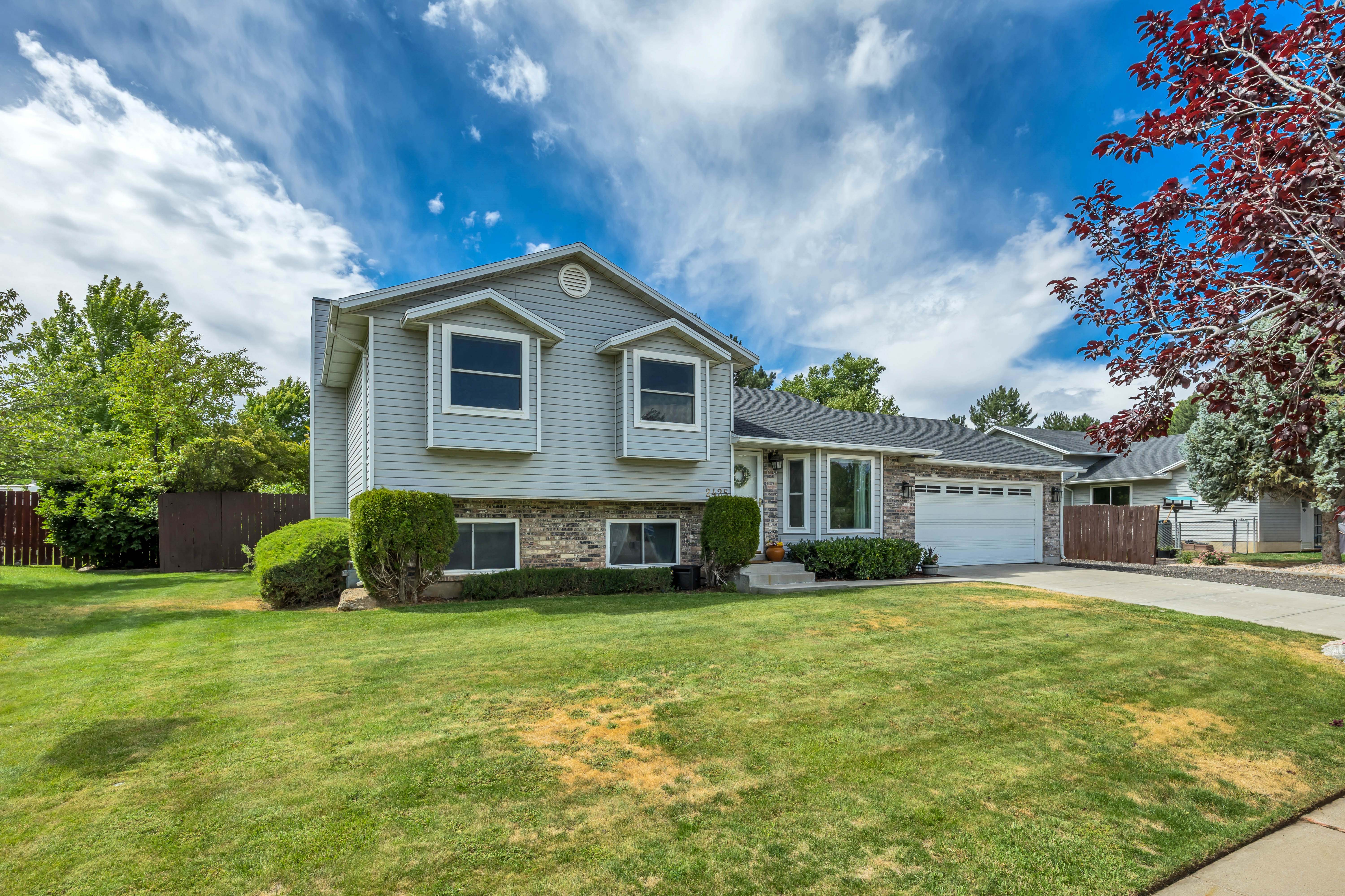 Split-level residence featuring light gray siding, brick accents, and a dark shingled roof