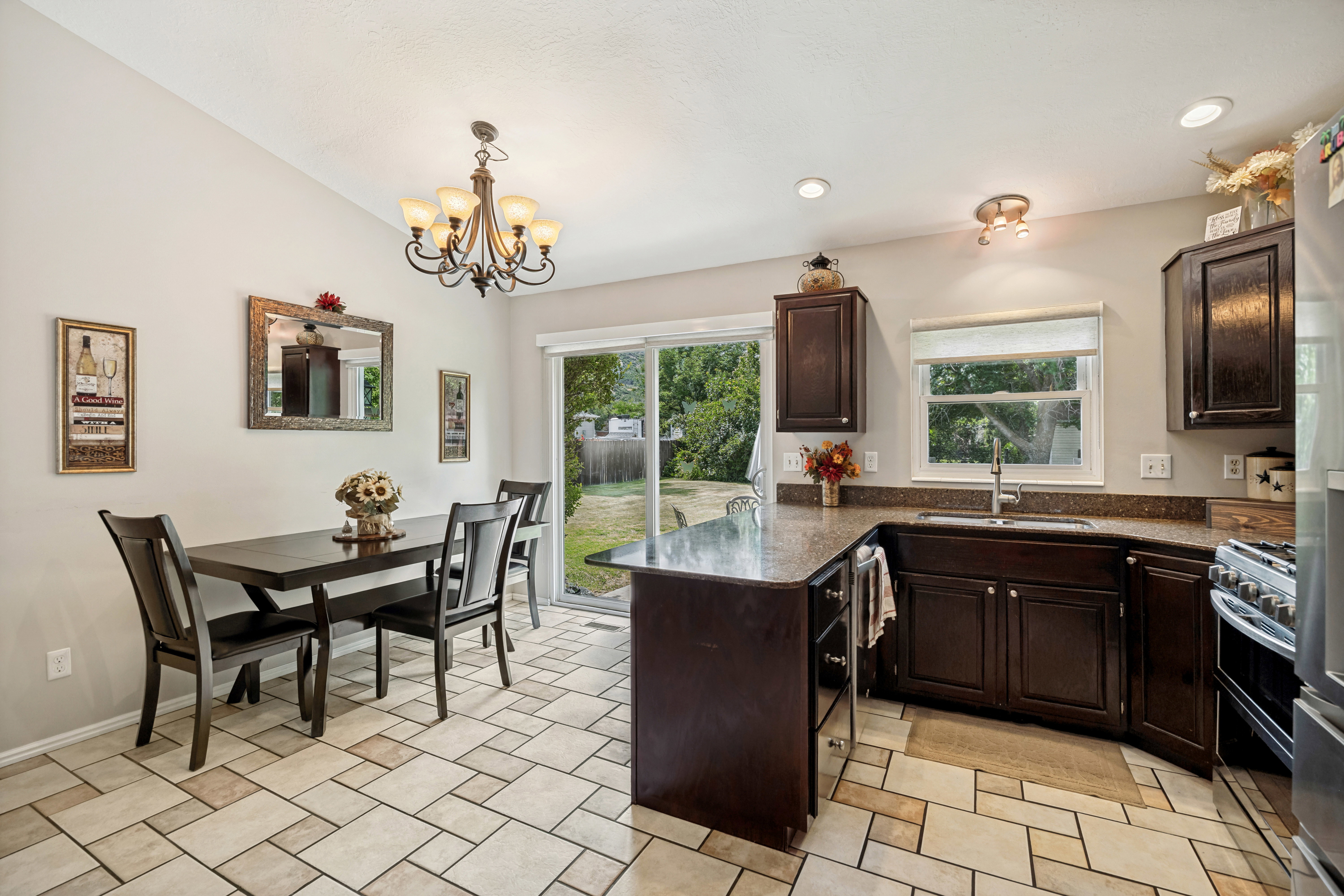 Kitchen and dining area featuring tile flooring, dark wood-finish cabinetry, granite-style countertops, a stainless steel sink, and a sliding glass door to the exterior