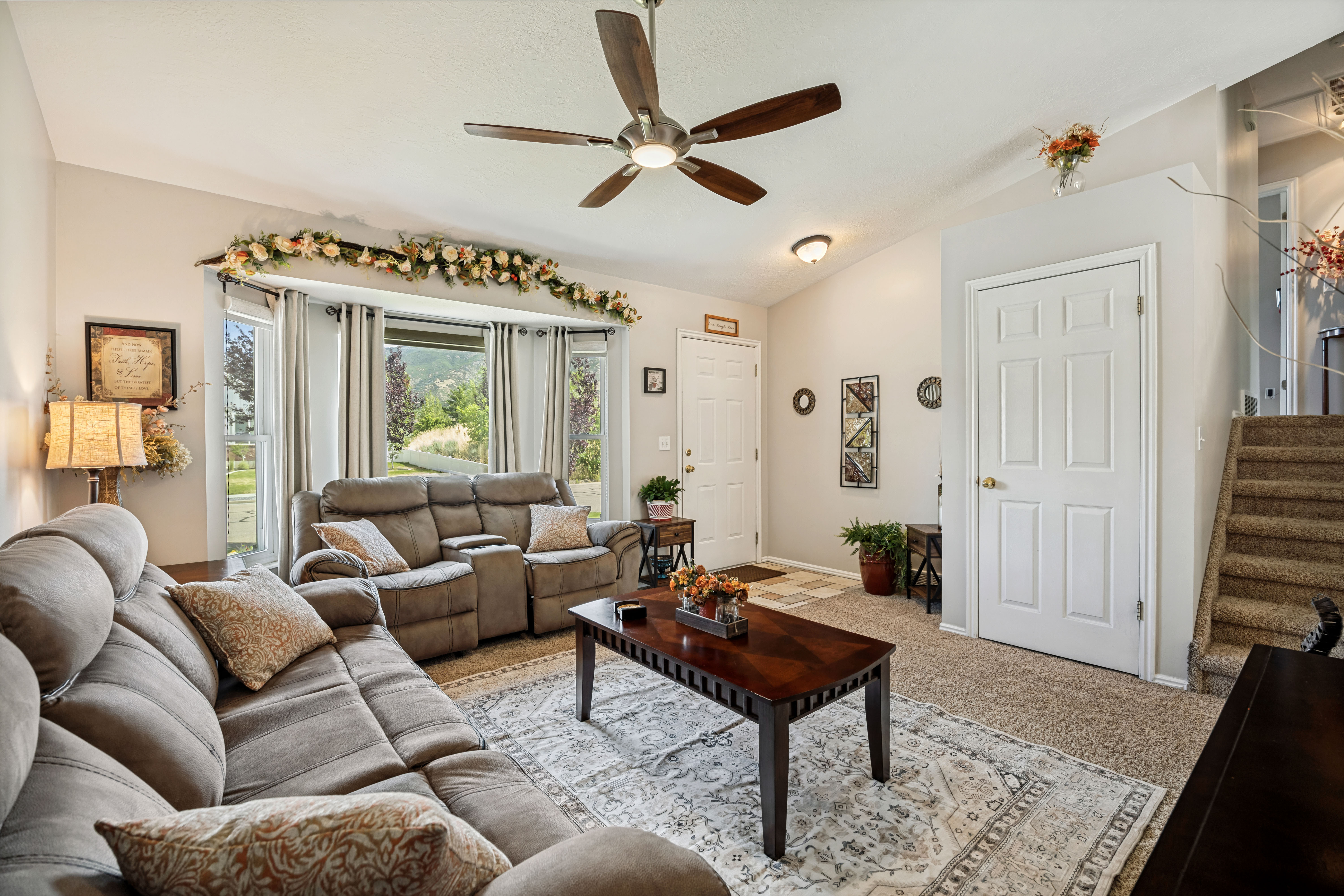 Spacious living area featuring a bay window, ceiling fan, and carpeted flooring