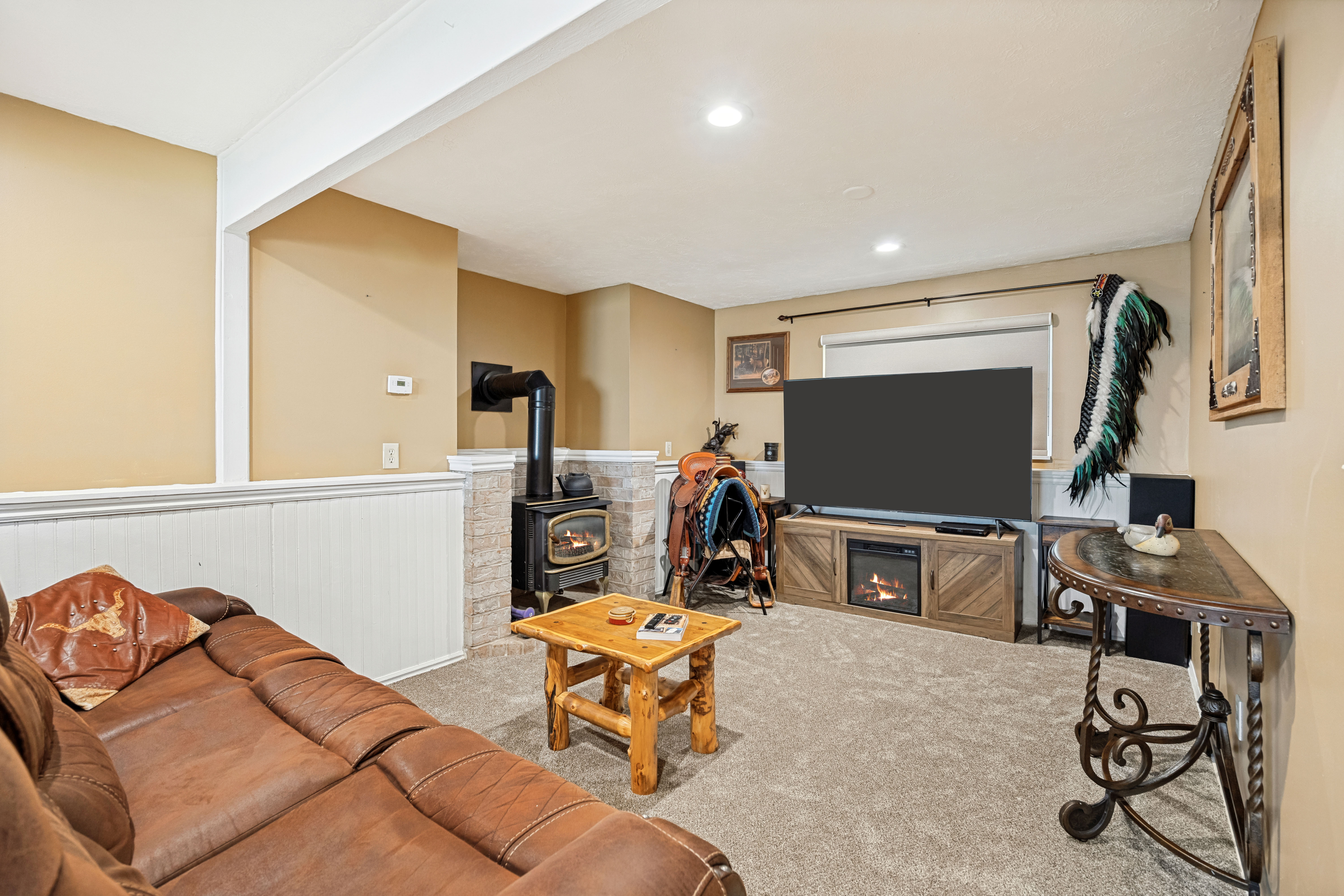 Carpeted area featuring a wood-burning stove with a stone surround, recessed lighting, and white wainscoting