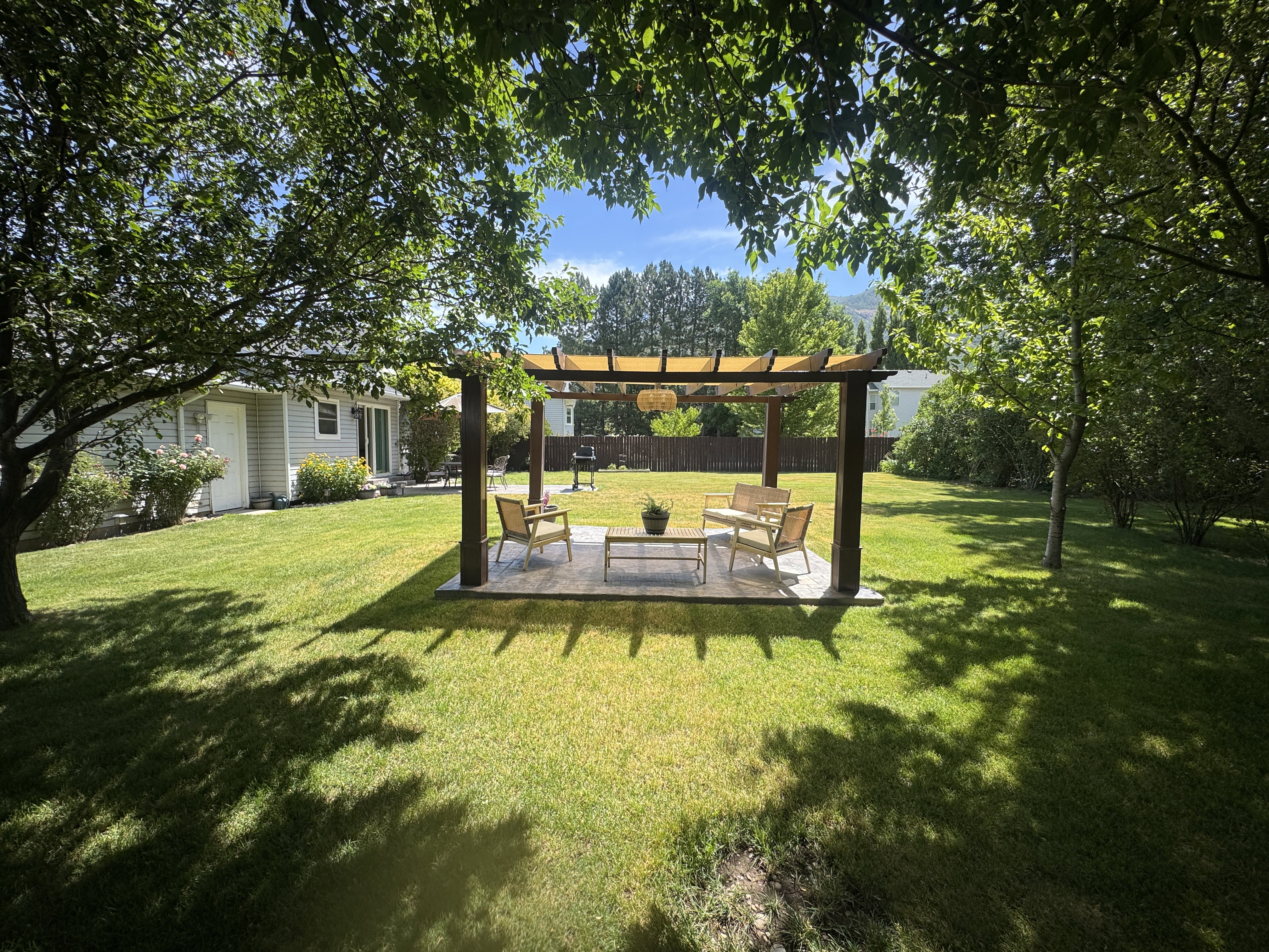 Expansive lawn featuring a wood pergola with a sunshade over a paved patio area