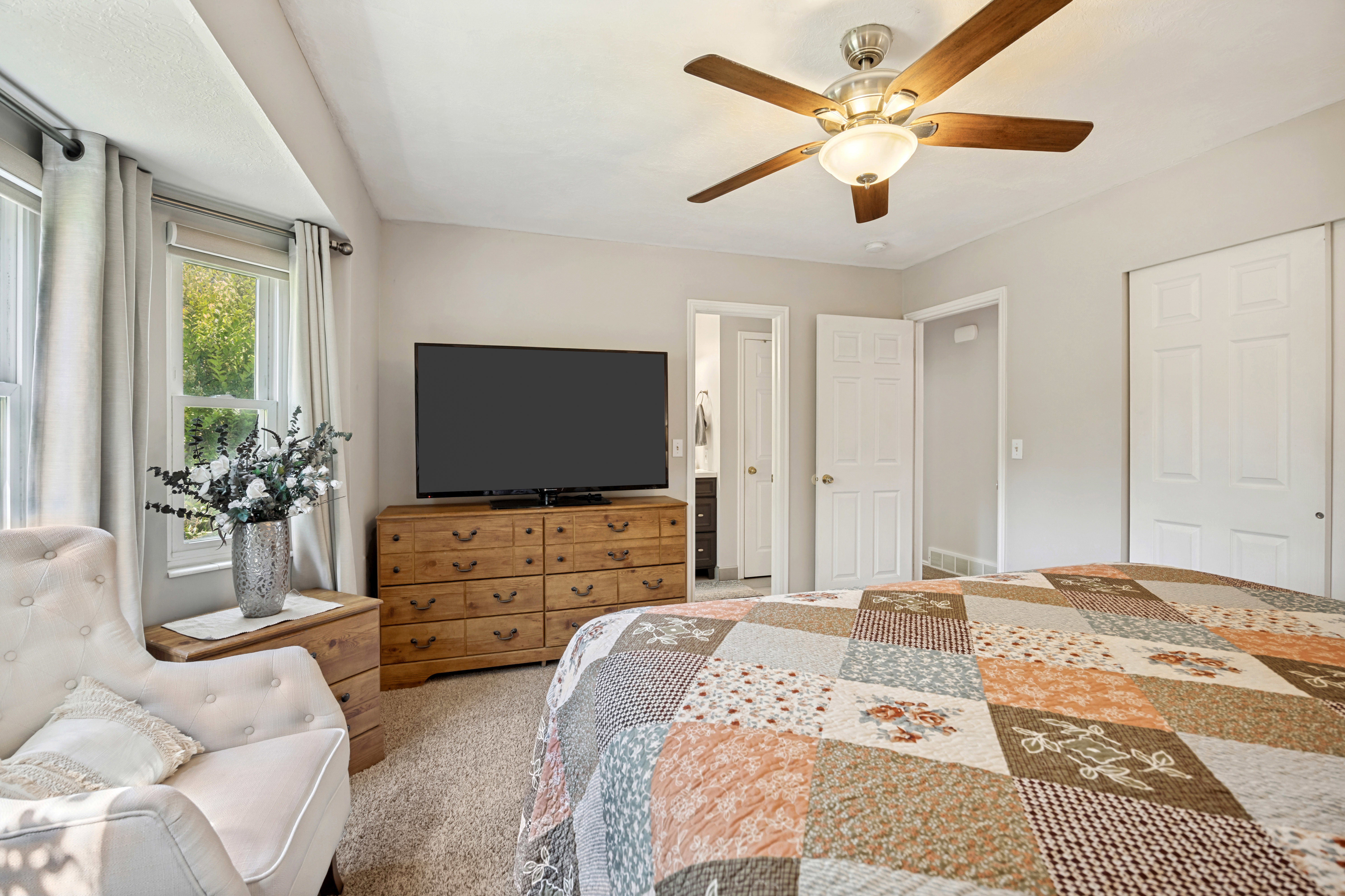 Carpeted room featuring a ceiling fan with wood-finish blades, a built-in closet with sliding doors, and a window with light-filtering curtains