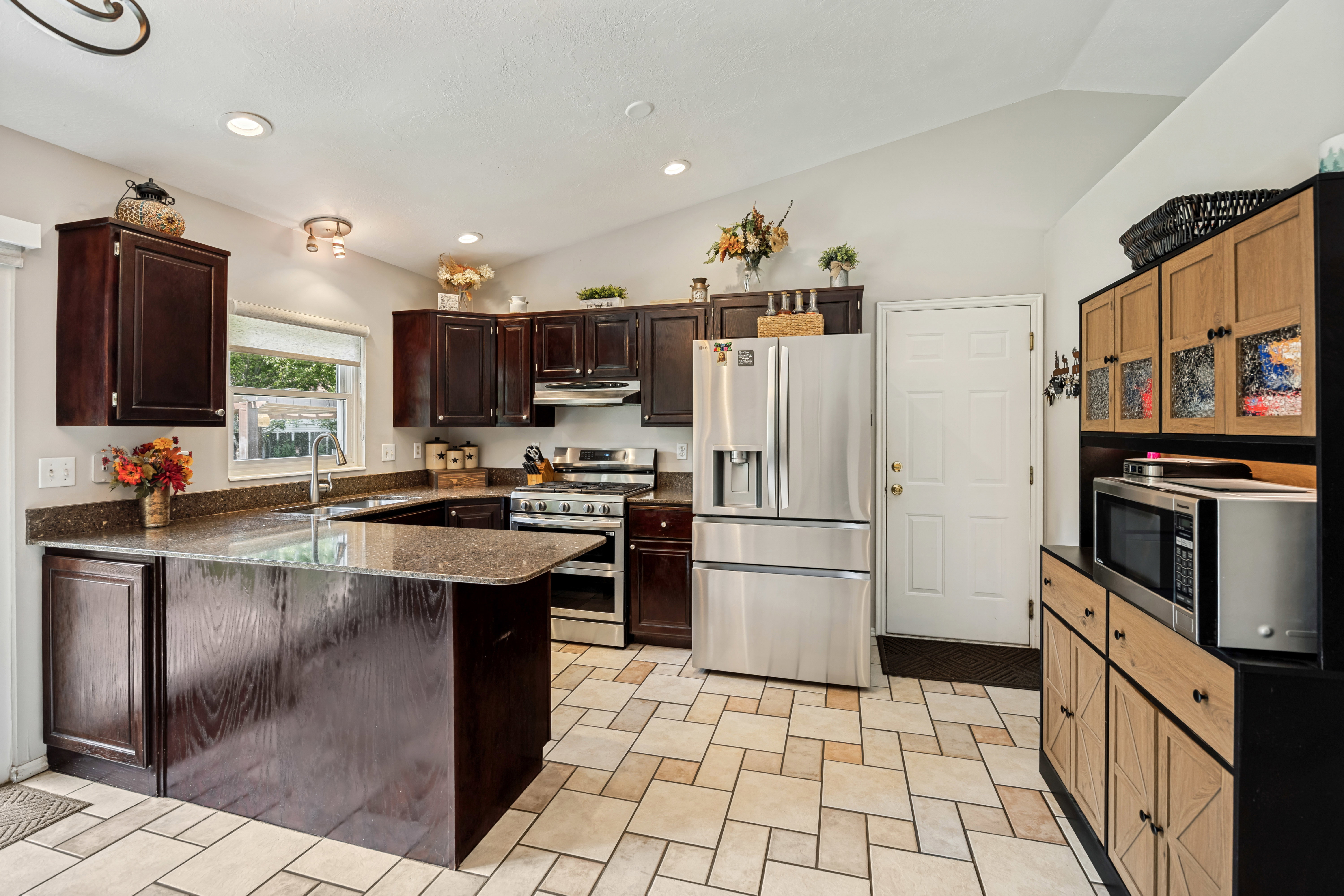 Open-concept kitchen featuring dark wood cabinetry, granite-style countertops, stainless steel appliances, and a central island with an integrated sink