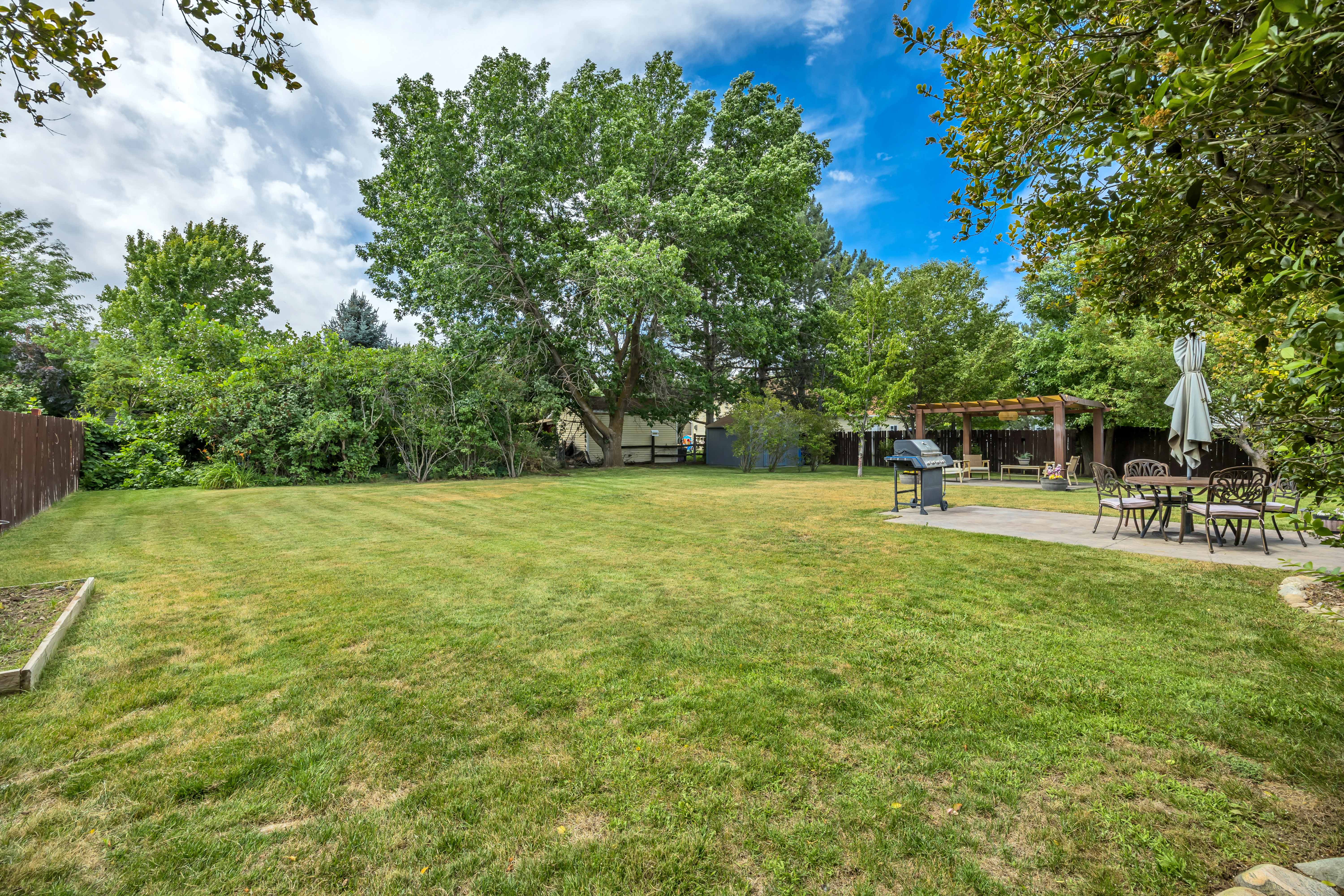 Spacious green lawn featuring a paved patio area, a wooden pergola, and mature trees