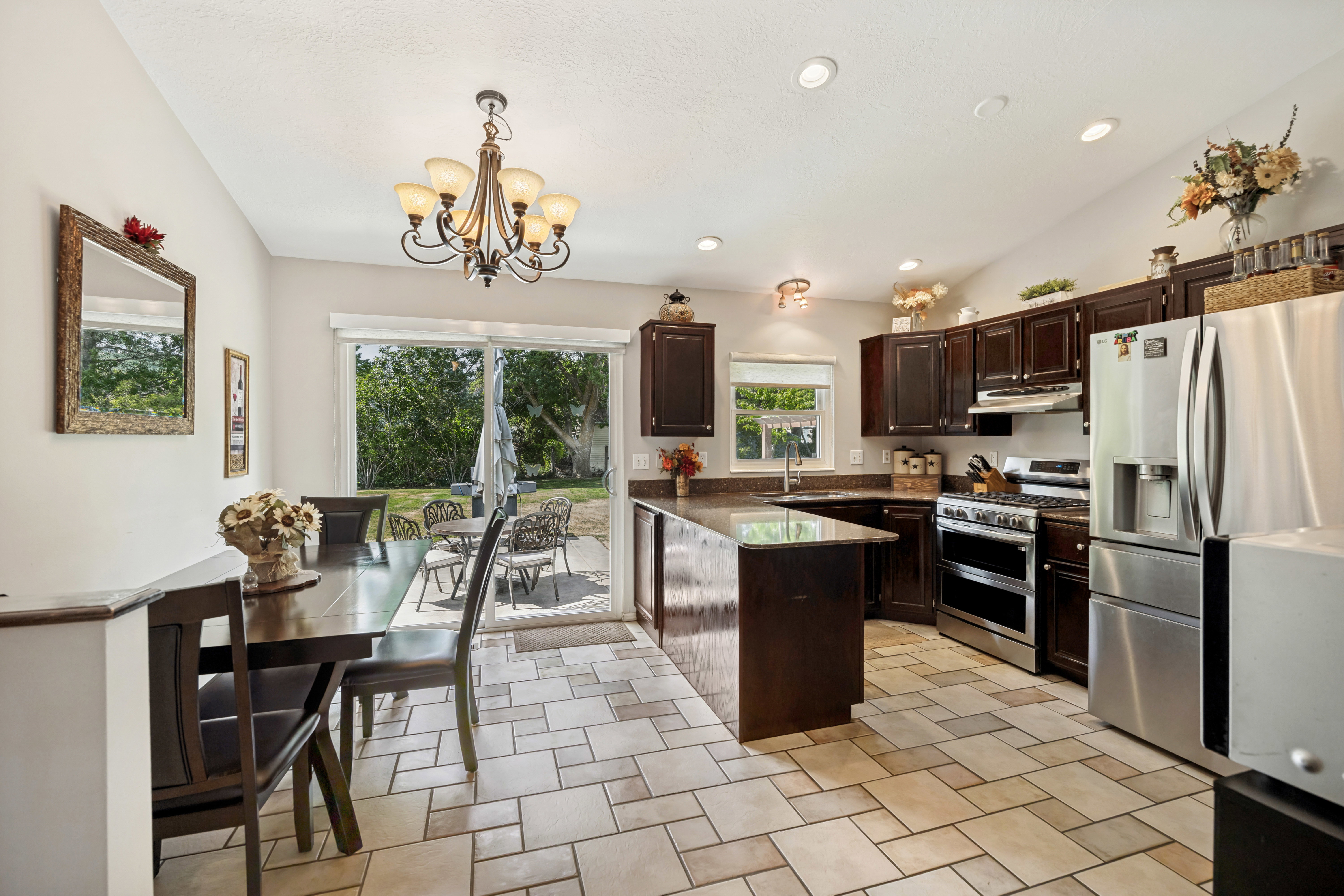 Open-concept kitchen and dining area featuring dark wood cabinetry, stainless steel appliances, a center island with countertop seating, and light-toned geometric tile flooring