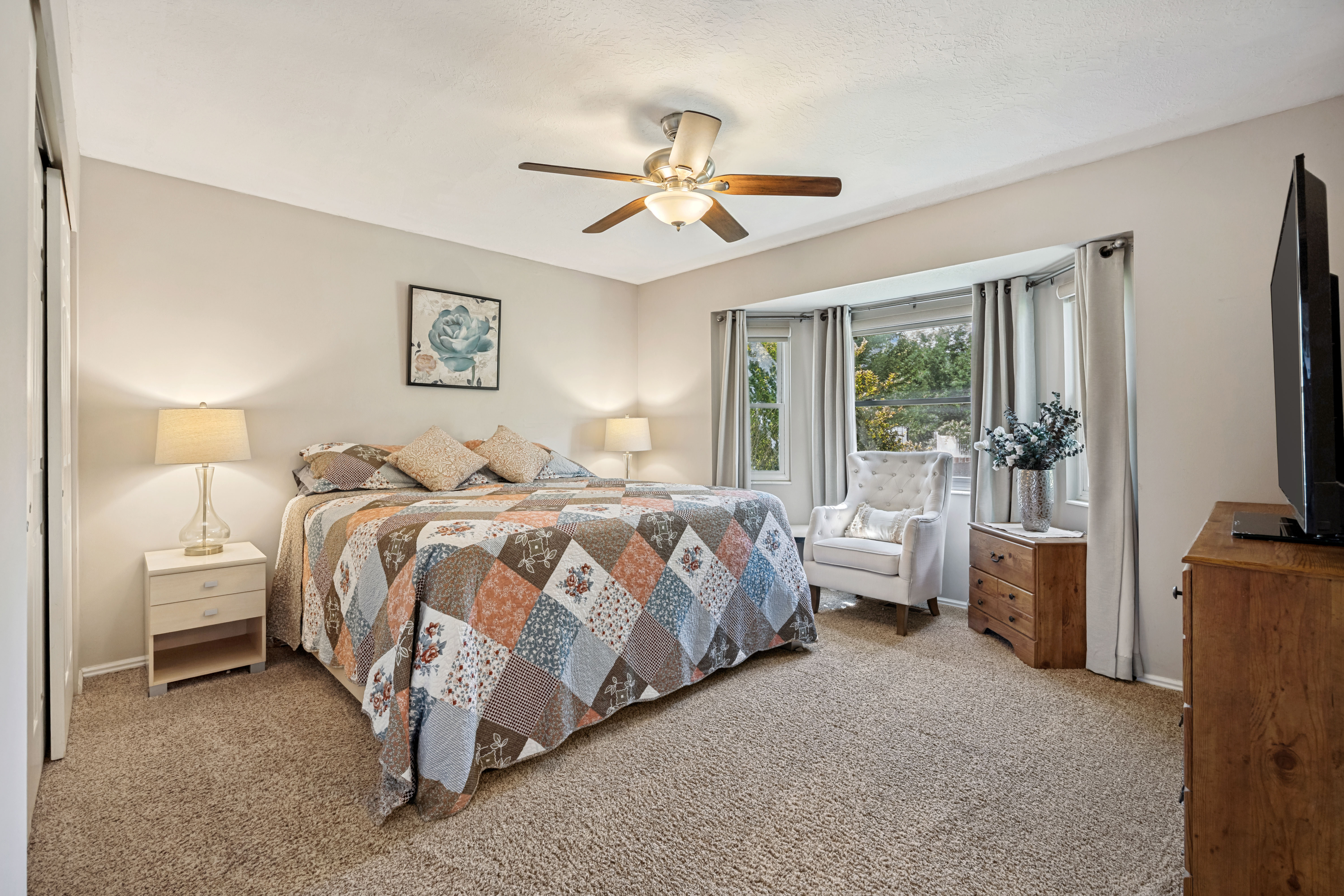 Carpeted room featuring a bay window, ceiling fan with light fixture, and neutral painted walls
