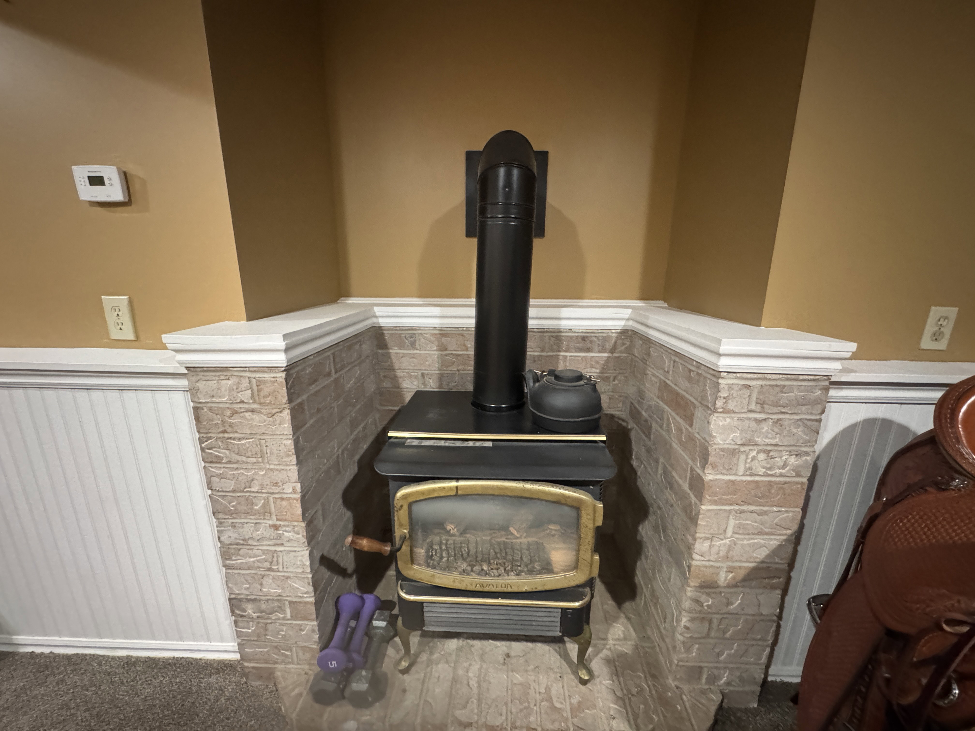 Corner wood-burning stove with a brick surround and hearth, featuring a black stovepipe