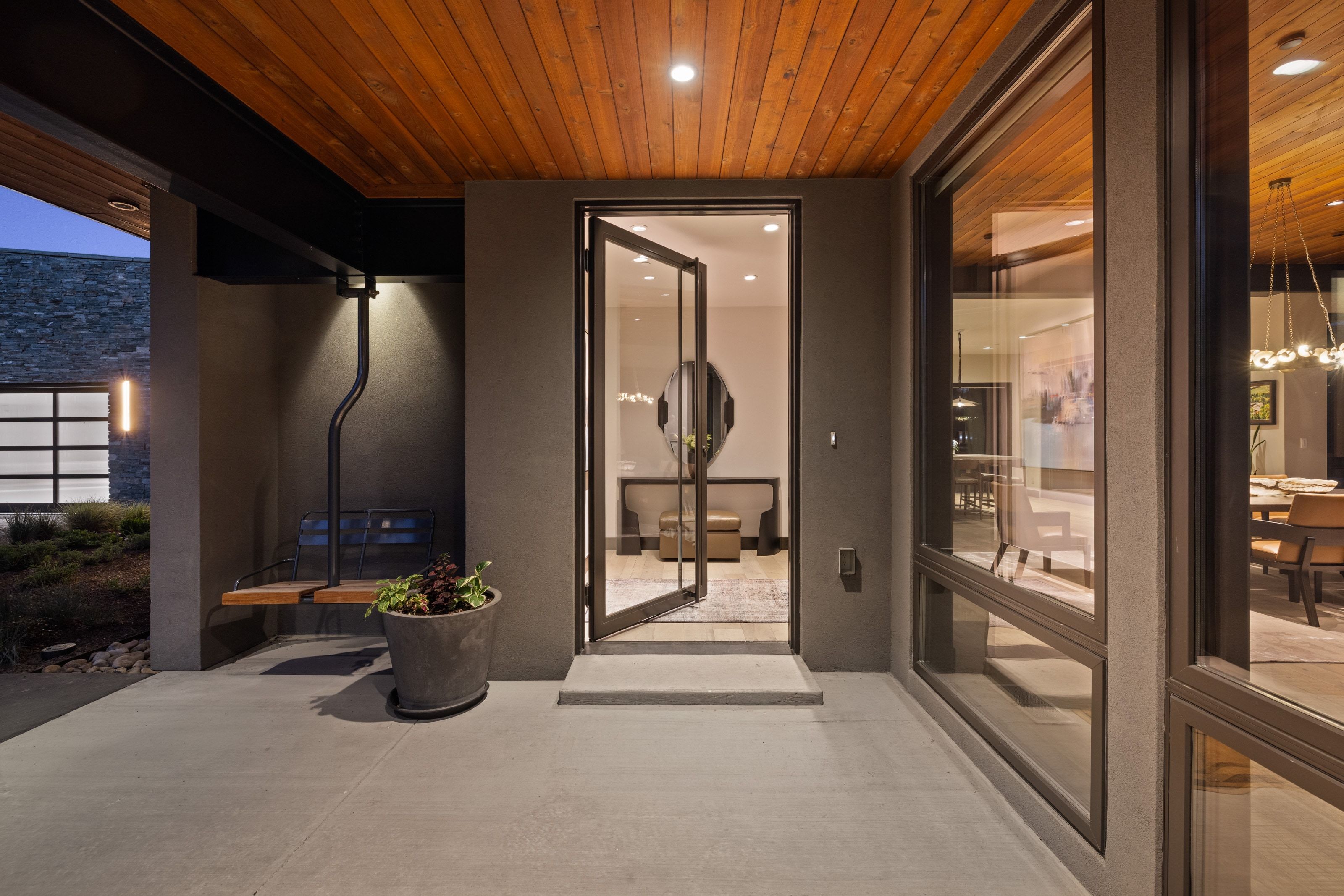 Modern entry featuring a wood-finish soffit, concrete patio, and dark-framed glass double doors