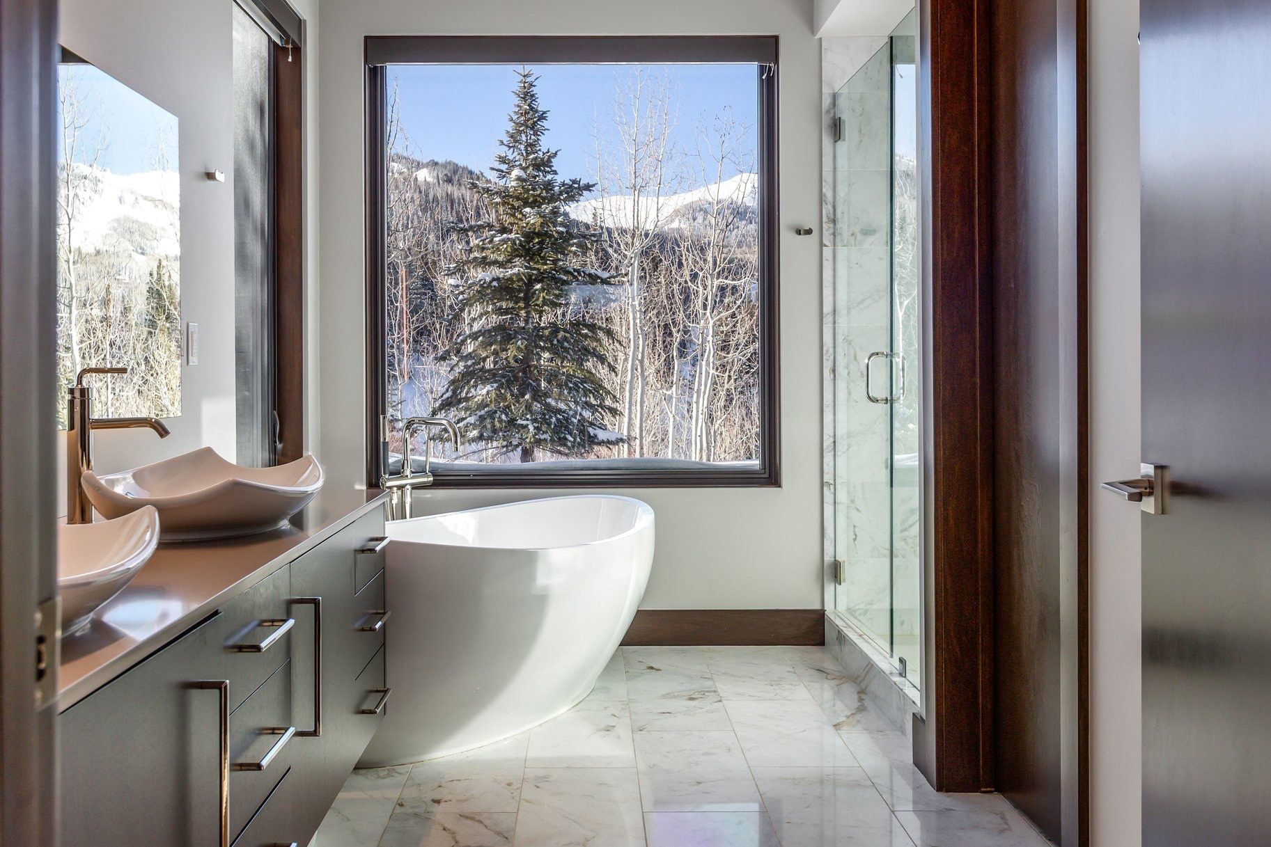 Contemporary bathroom featuring a freestanding soaking tub, dual vessel sinks with wall-mounted faucets, a glass-enclosed shower, and marble flooring