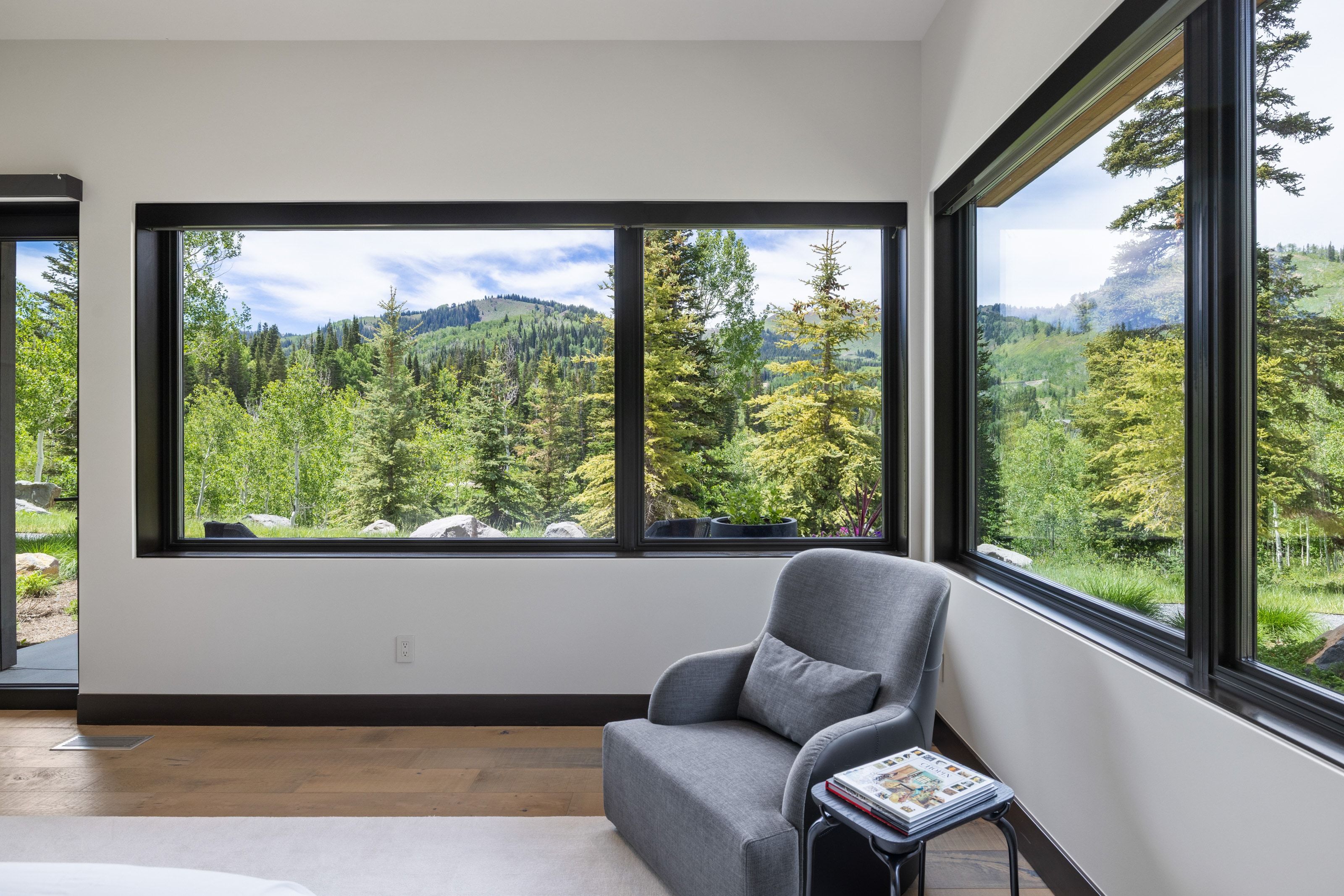 Expansive windows with black framing showcasing a mountainous and wooded landscape