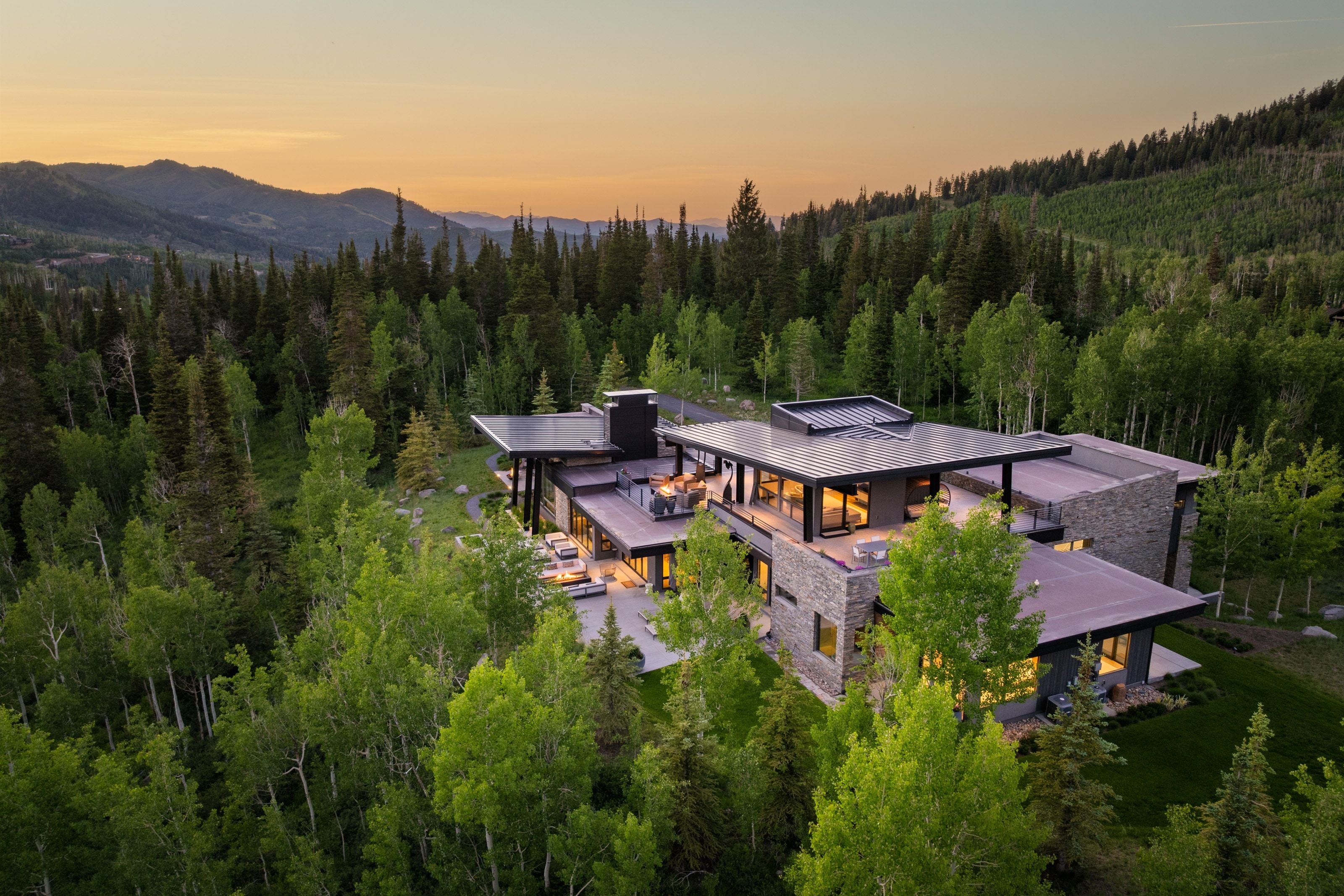 Modern architectural residence featuring stone and dark siding, multiple outdoor patios, and expansive windows