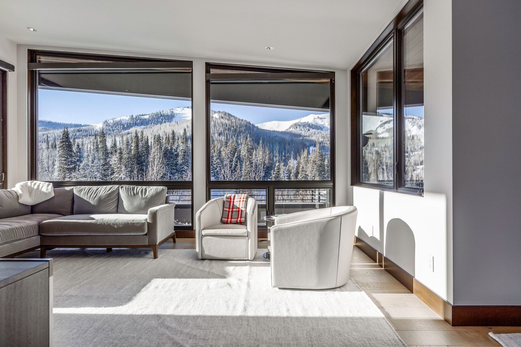 Expansive windows showcasing mountain scenery, complemented by recessed lighting, light-toned flooring, and dark window frames