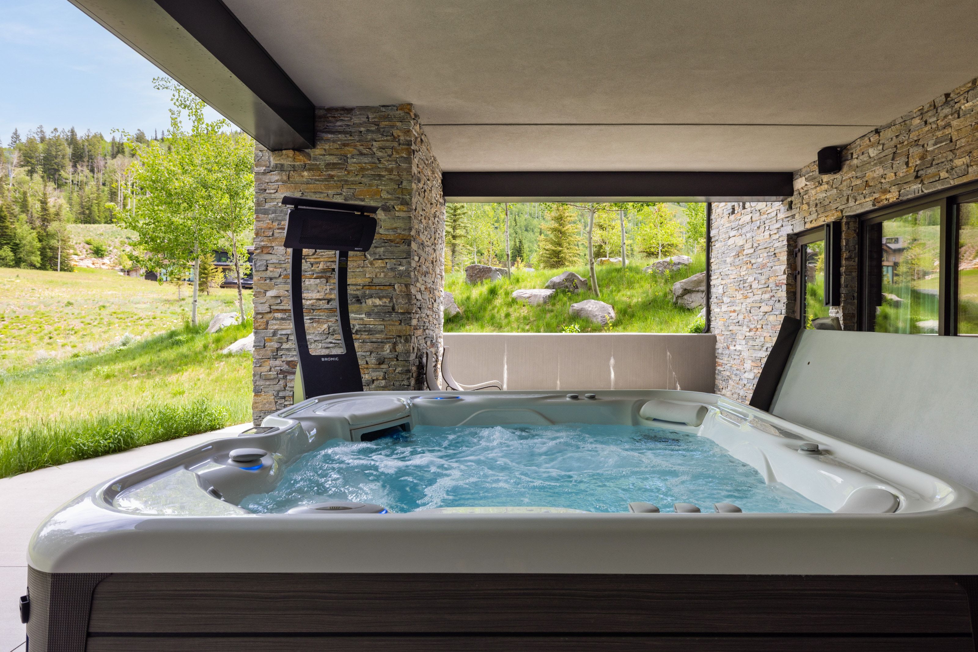 Covered outdoor patio featuring a built-in hot tub, stacked stone columns, and expansive glass doors