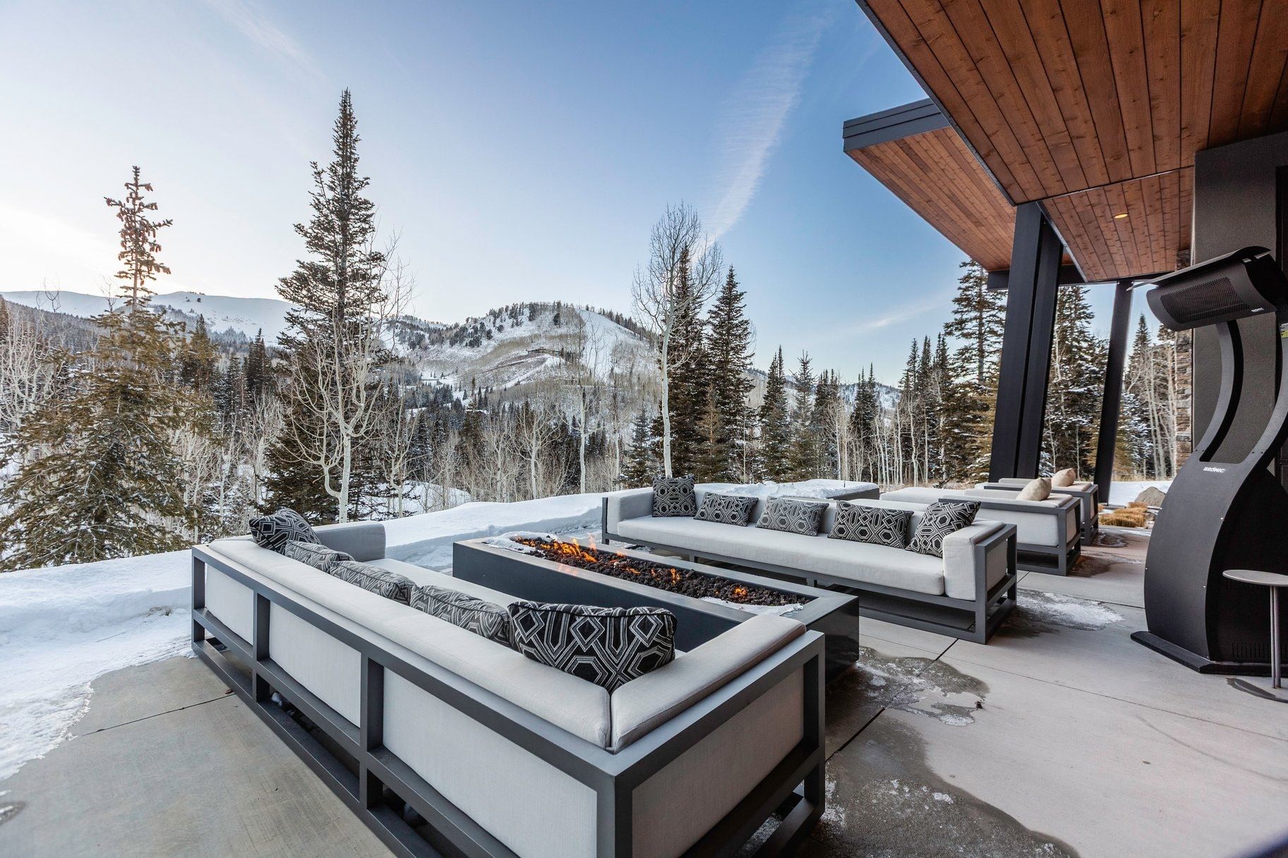 Expansive outdoor patio featuring a built-in fire pit, multiple seating areas, a wood-paneled ceiling, and a concrete surface