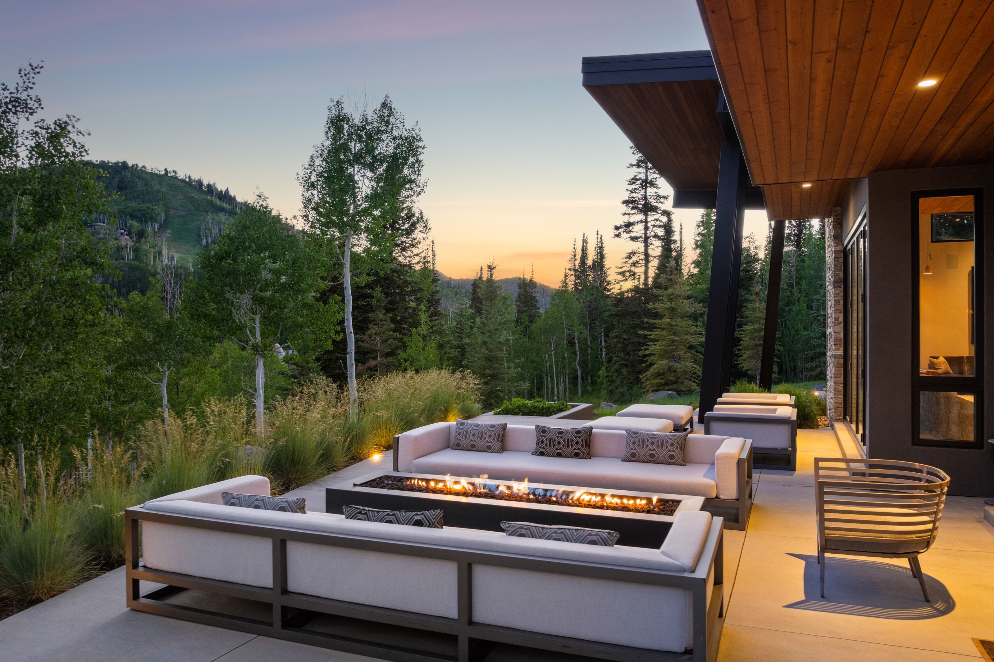 Spacious outdoor patio featuring a linear fire pit, concrete surface, and mature landscaping