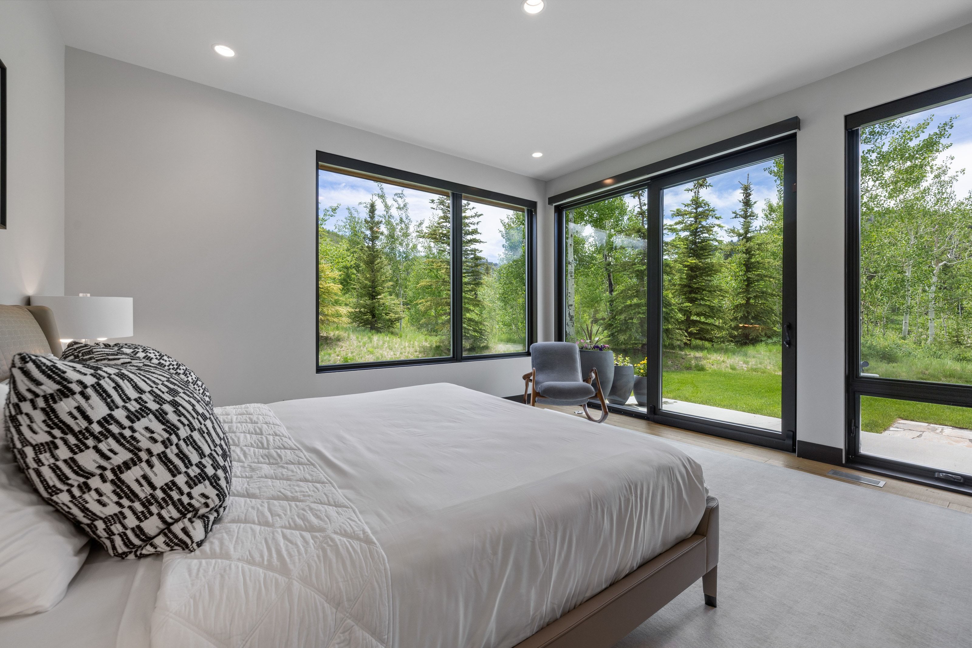 Floor-to-ceiling windows with black frames, recessed ceiling lighting, a light gray wall finish, and wood-finish flooring