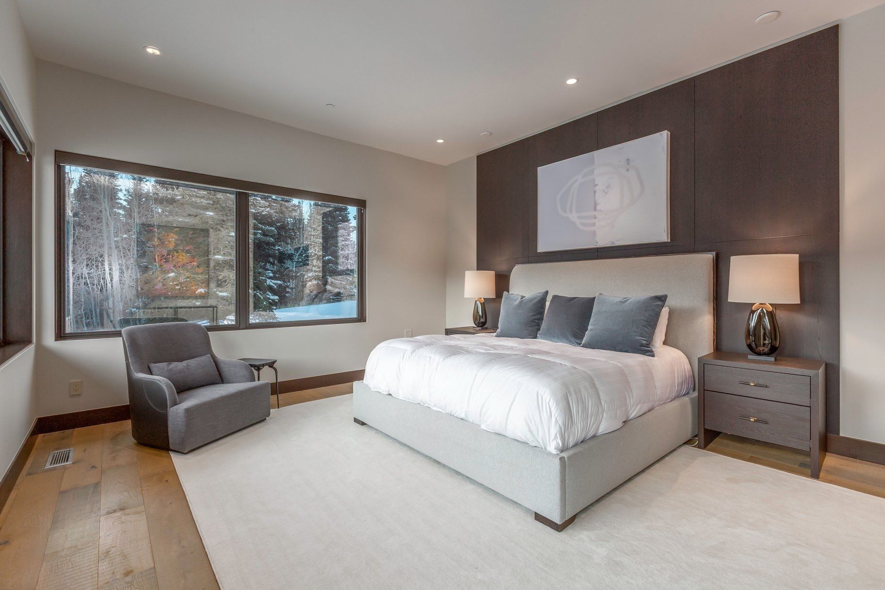 Expansive bedroom featuring large windows, wood-finish flooring, recessed lighting, and a textured accent wall