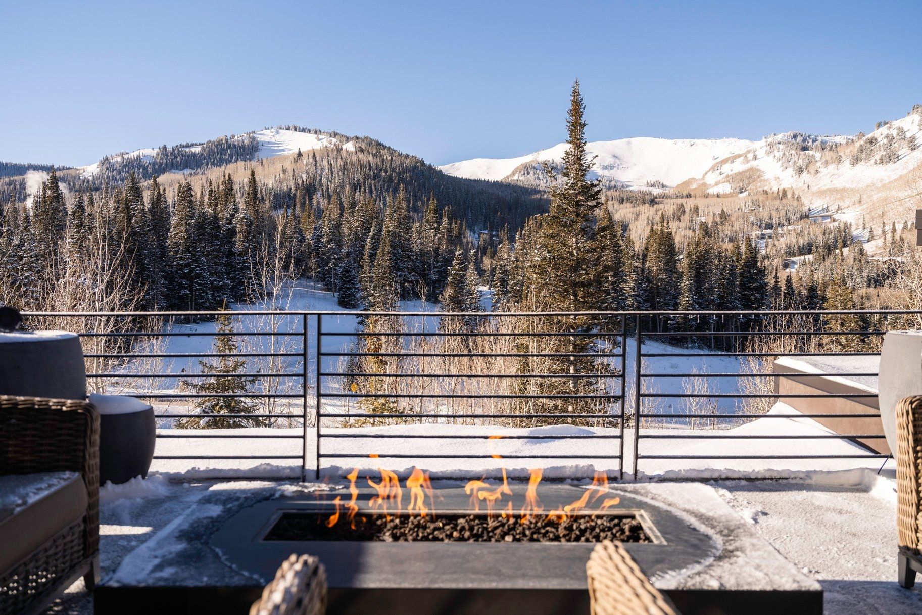 Outdoor patio featuring a built-in fire pit, metal railing, and snow-dusted natural landscape