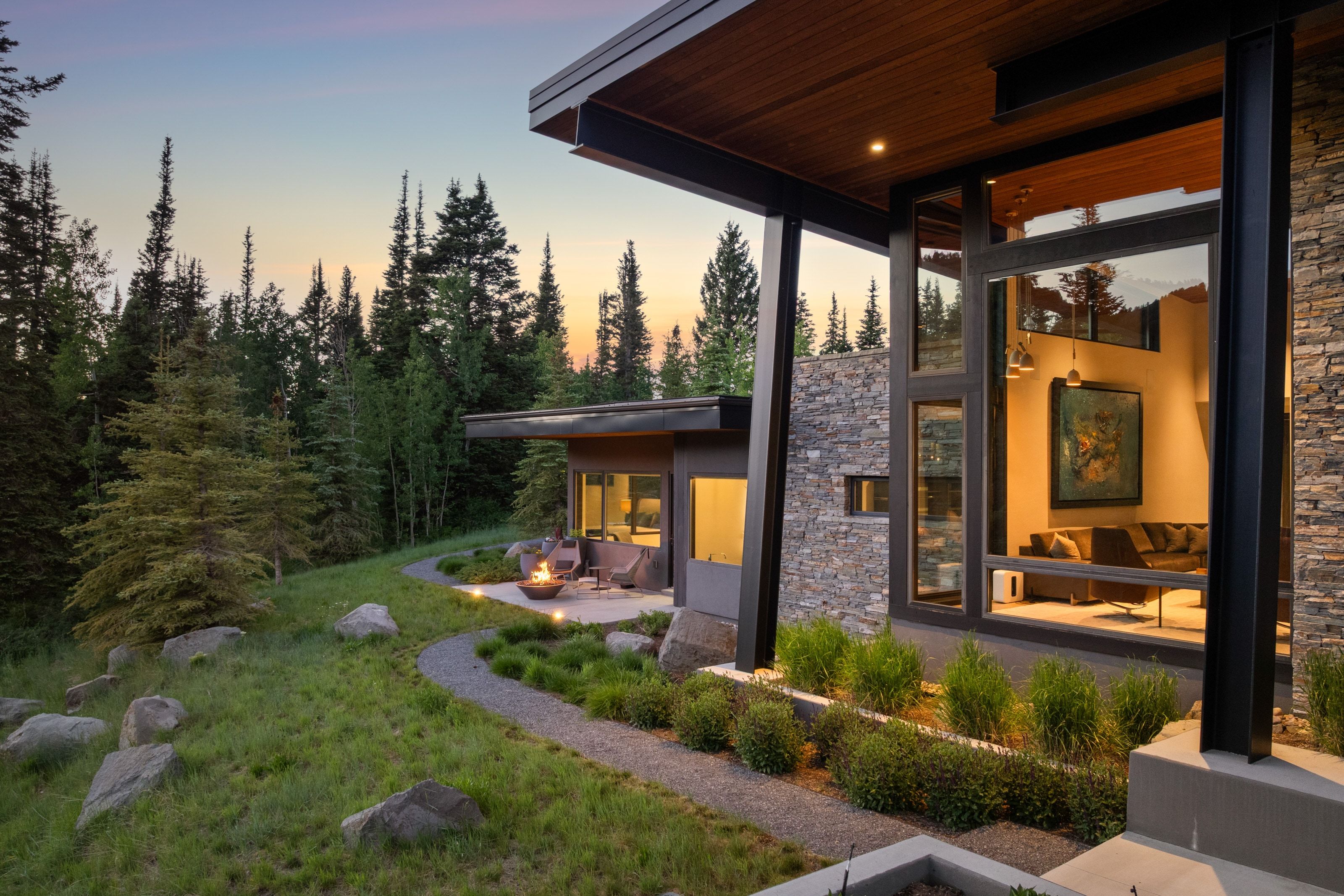 Modern architectural design featuring expansive window walls, a stone veneer exterior, a wood-finish soffit, and a patterned gravel pathway