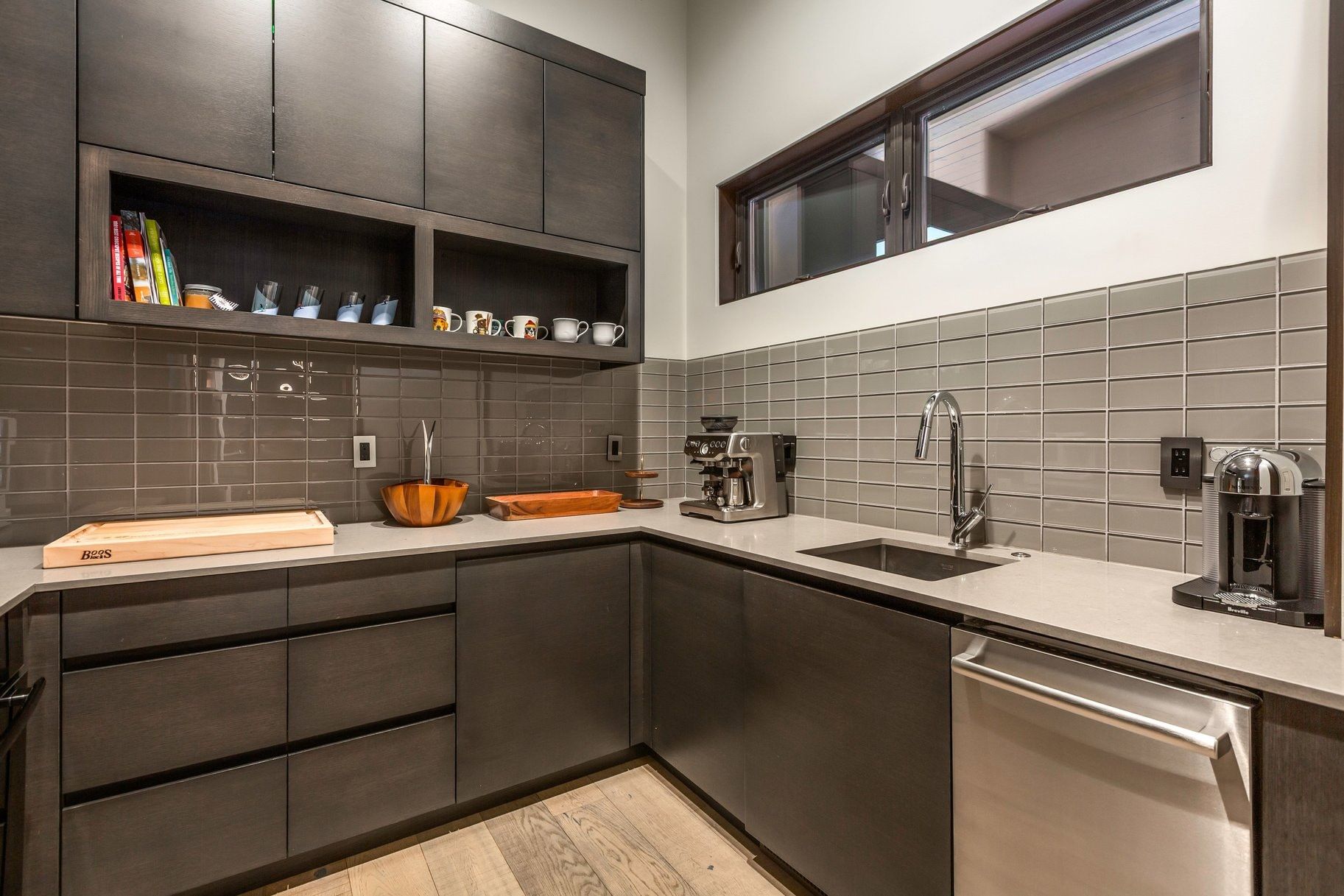 Contemporary kitchen featuring dark wood-finish cabinetry, light-toned countertops, subway tile backsplash, and a stainless steel dishwasher