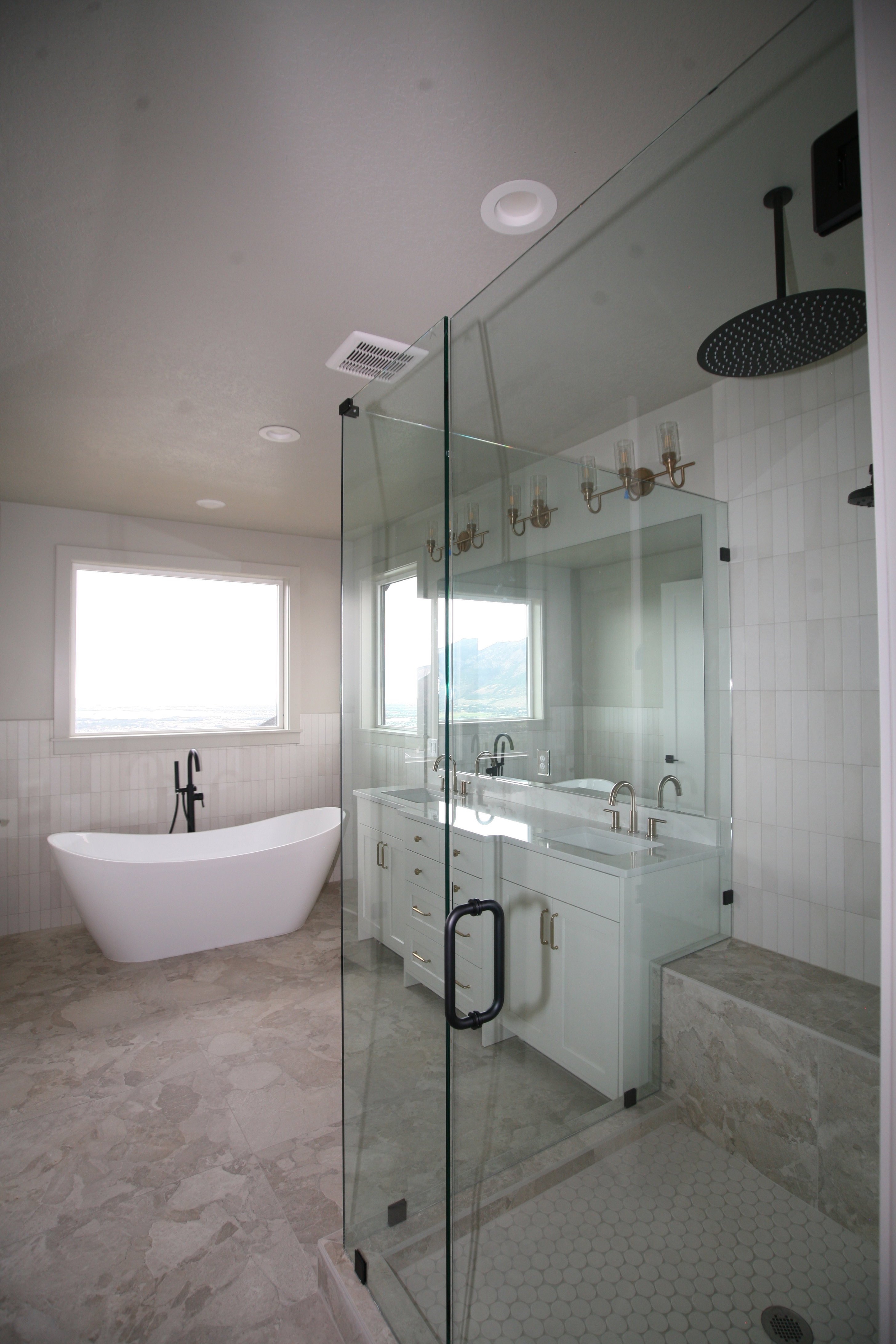 Spacious bathroom featuring a frameless glass shower enclosure, a dual vanity with white cabinetry, a freestanding soaking tub, and large format floor tiling