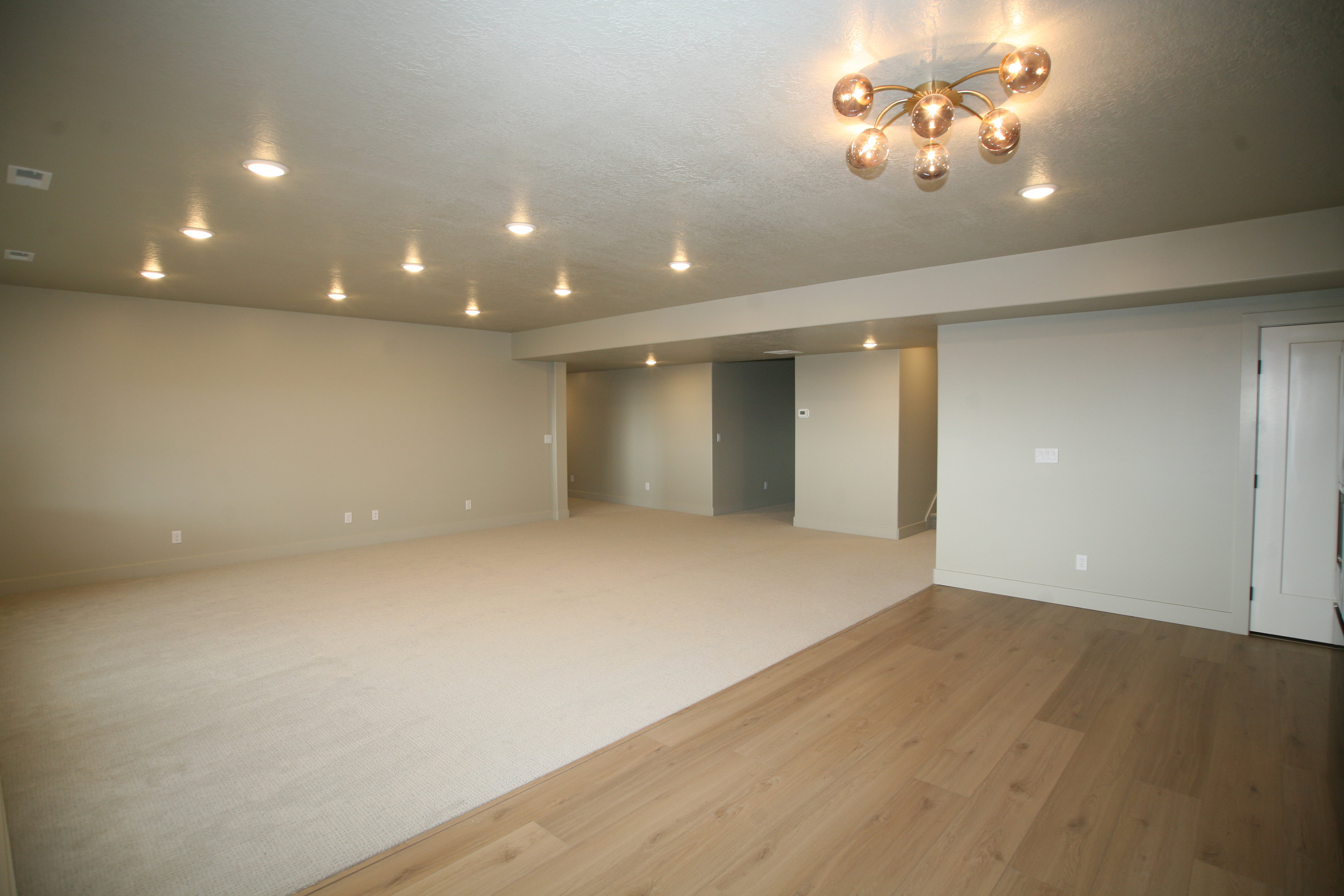 Spacious room featuring a contemporary chandelier, recessed lighting, and a combination of light-toned carpeting and wood-finish flooring