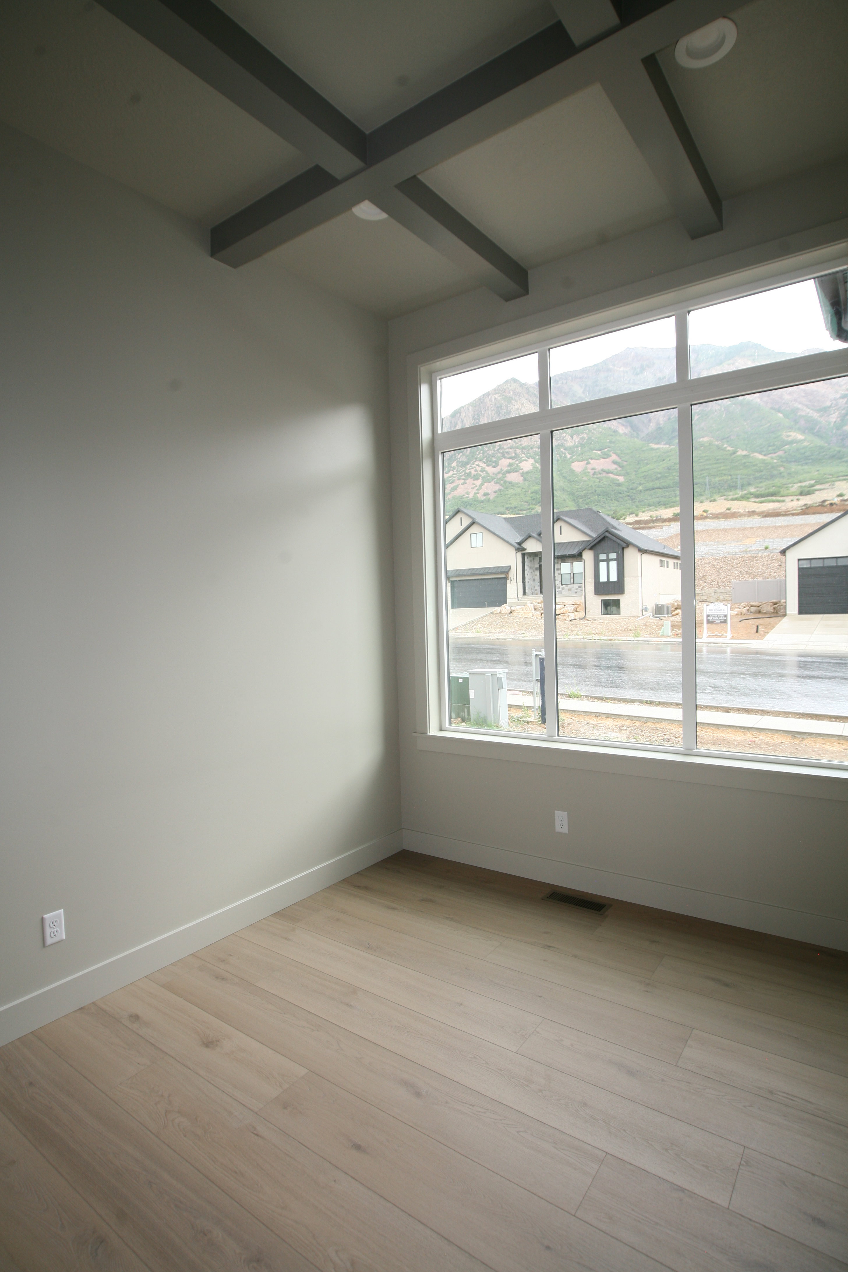 Spacious room featuring a large multi-pane window, light wood-finish flooring, and a coffered ceiling with recessed lighting