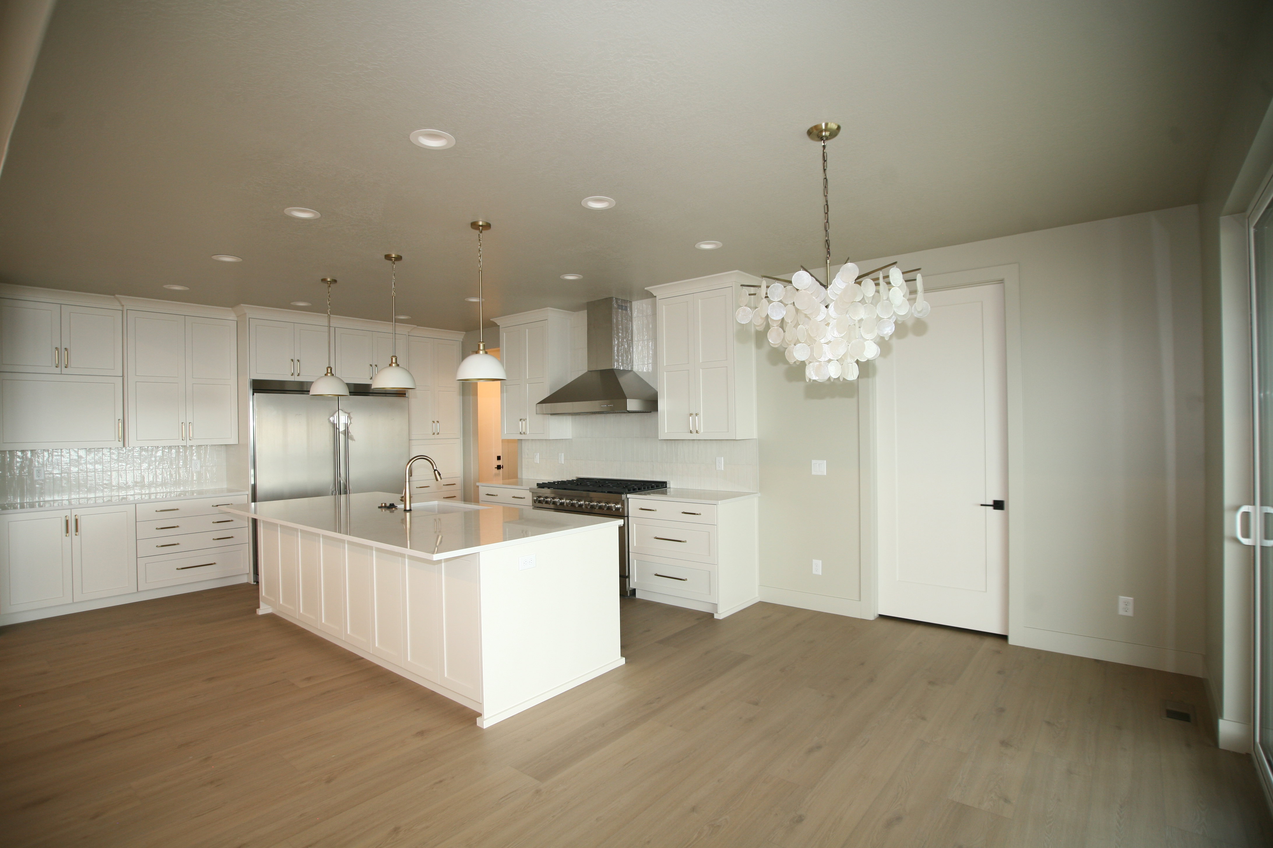 Spacious kitchen featuring an expansive center island with an undermount sink, white cabinetry, integrated stainless steel refrigerator, professional-grade range with a stainless steel hood, and wood-finish flooring
