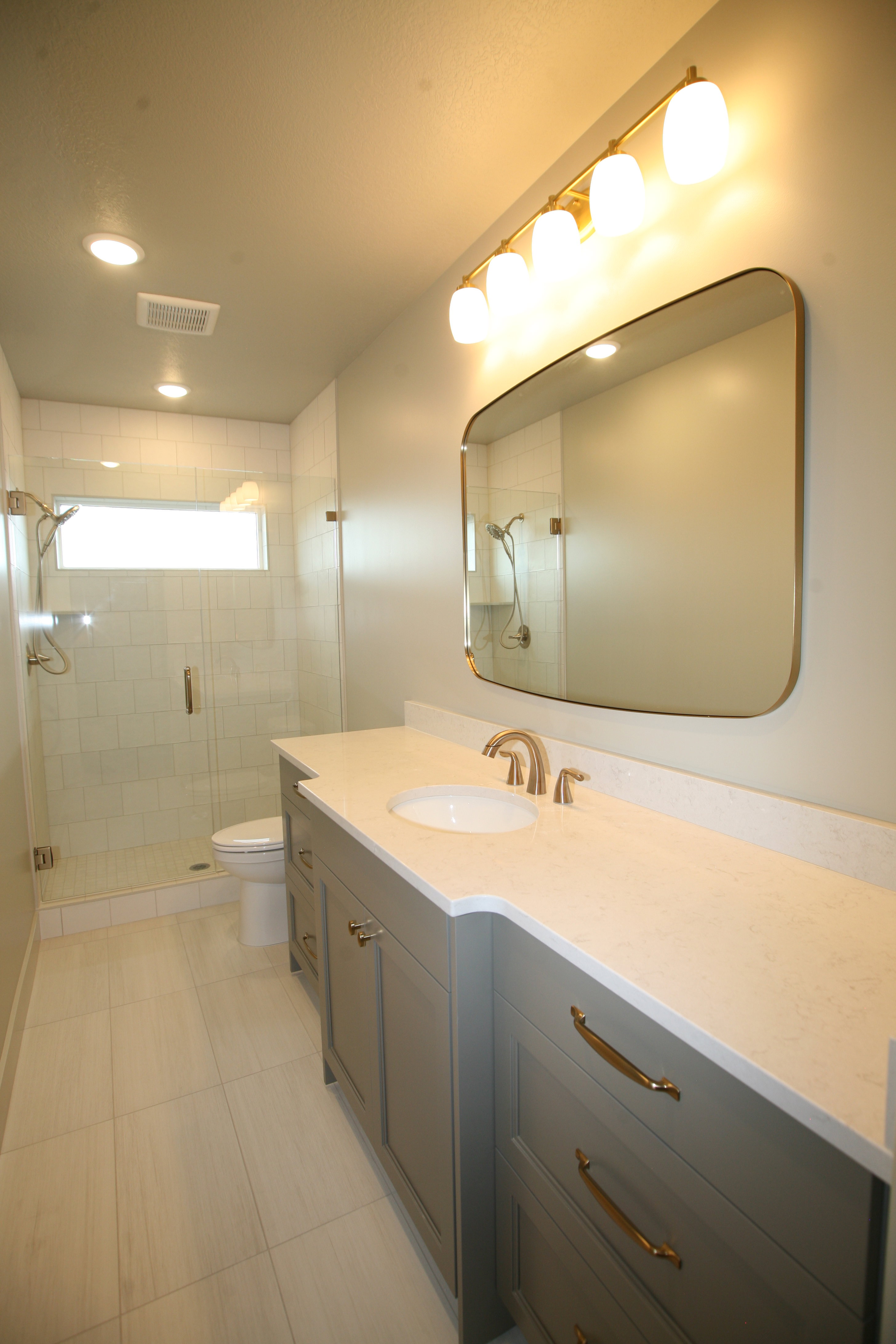 Bathroom featuring a double vanity with light gray cabinetry, white countertop, and gold-toned hardware