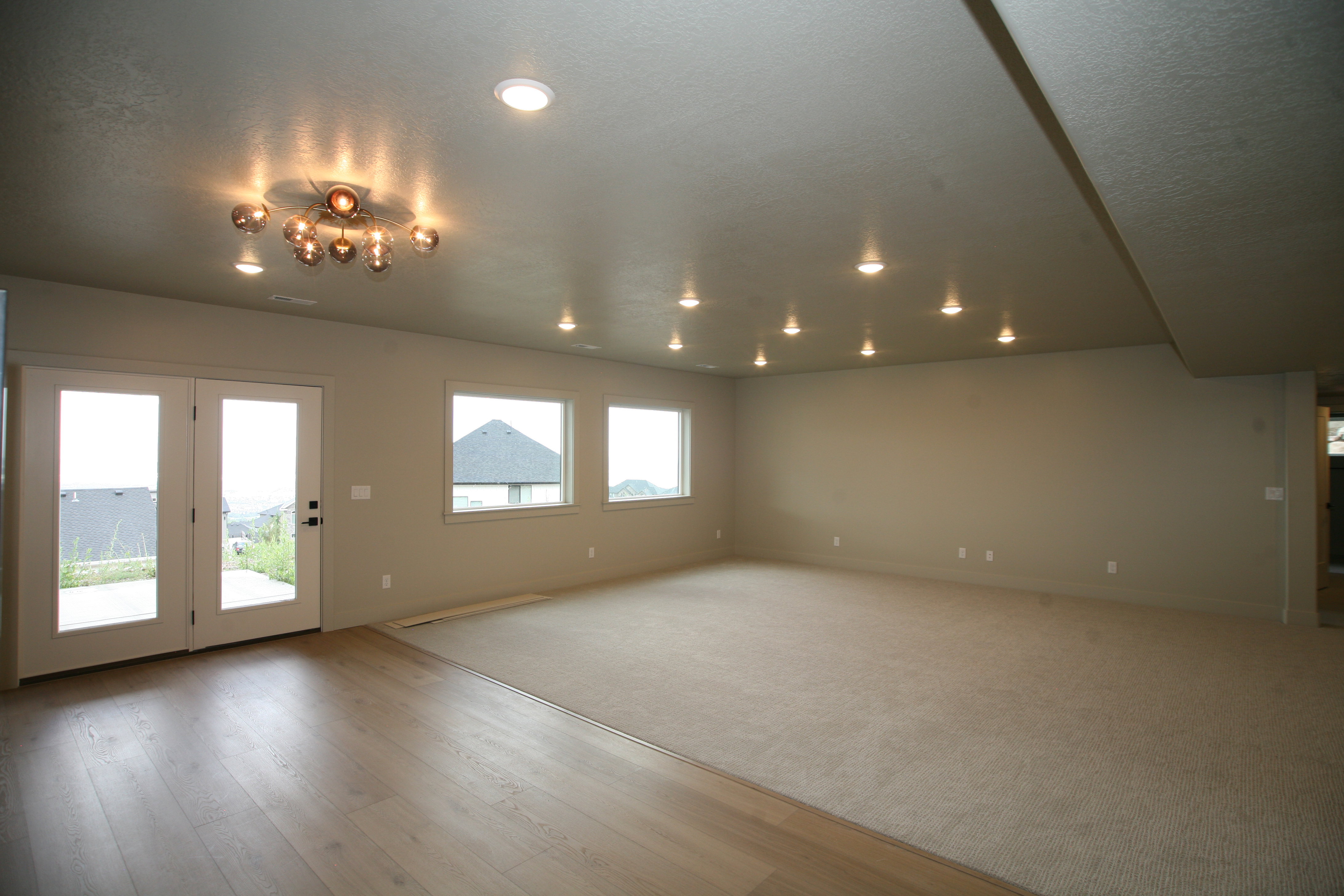Spacious room featuring a contemporary multi-bulb ceiling fixture, multiple recessed lights, and a combination of light wood-finish flooring and neutral carpeting